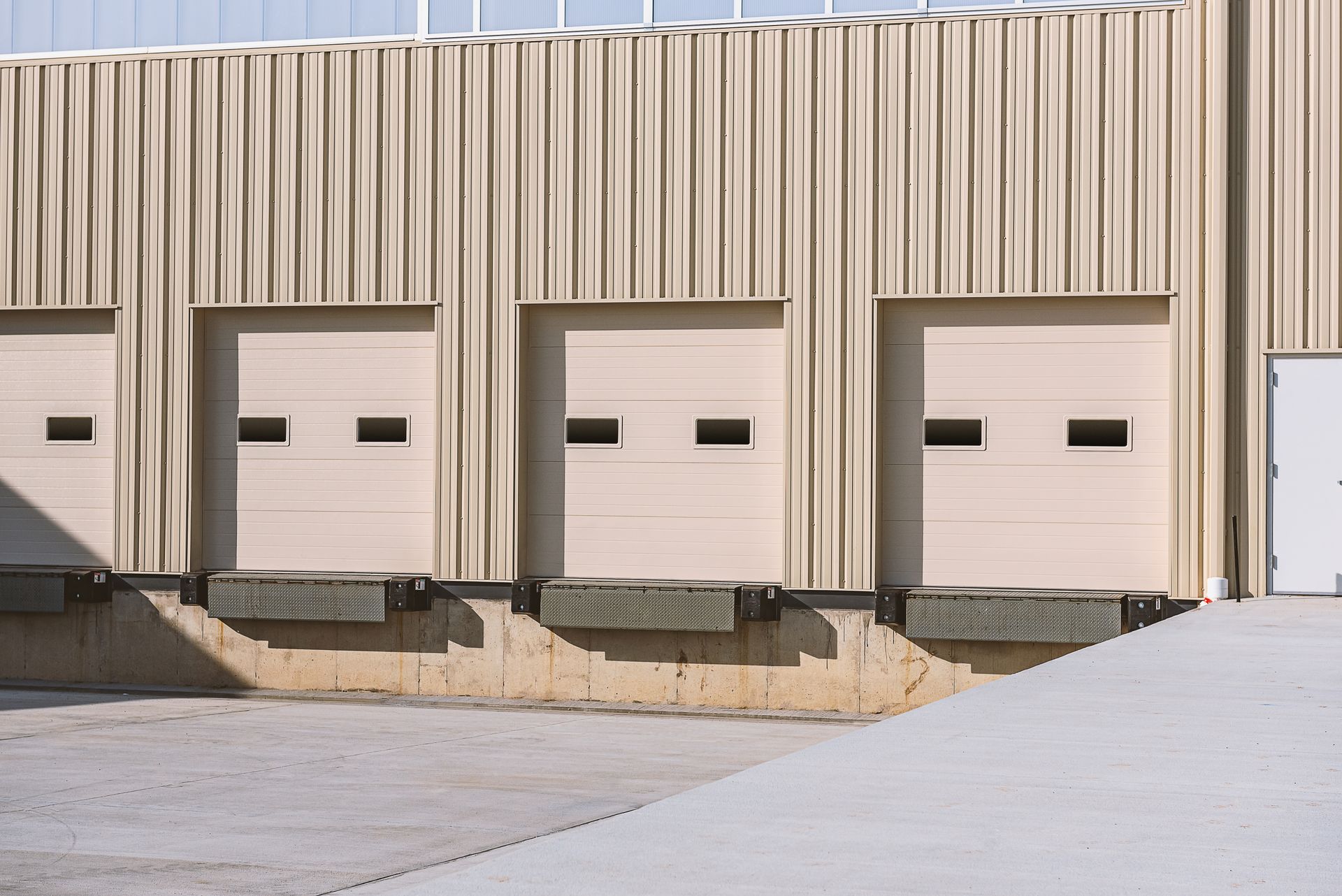 Industrial loading docks with four beige garage doors on a beige warehouse building