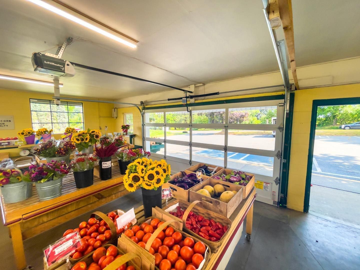 Flower and fruit stand inside a garage, with buckets of colorful blooms and crates of fresh produce by an open door