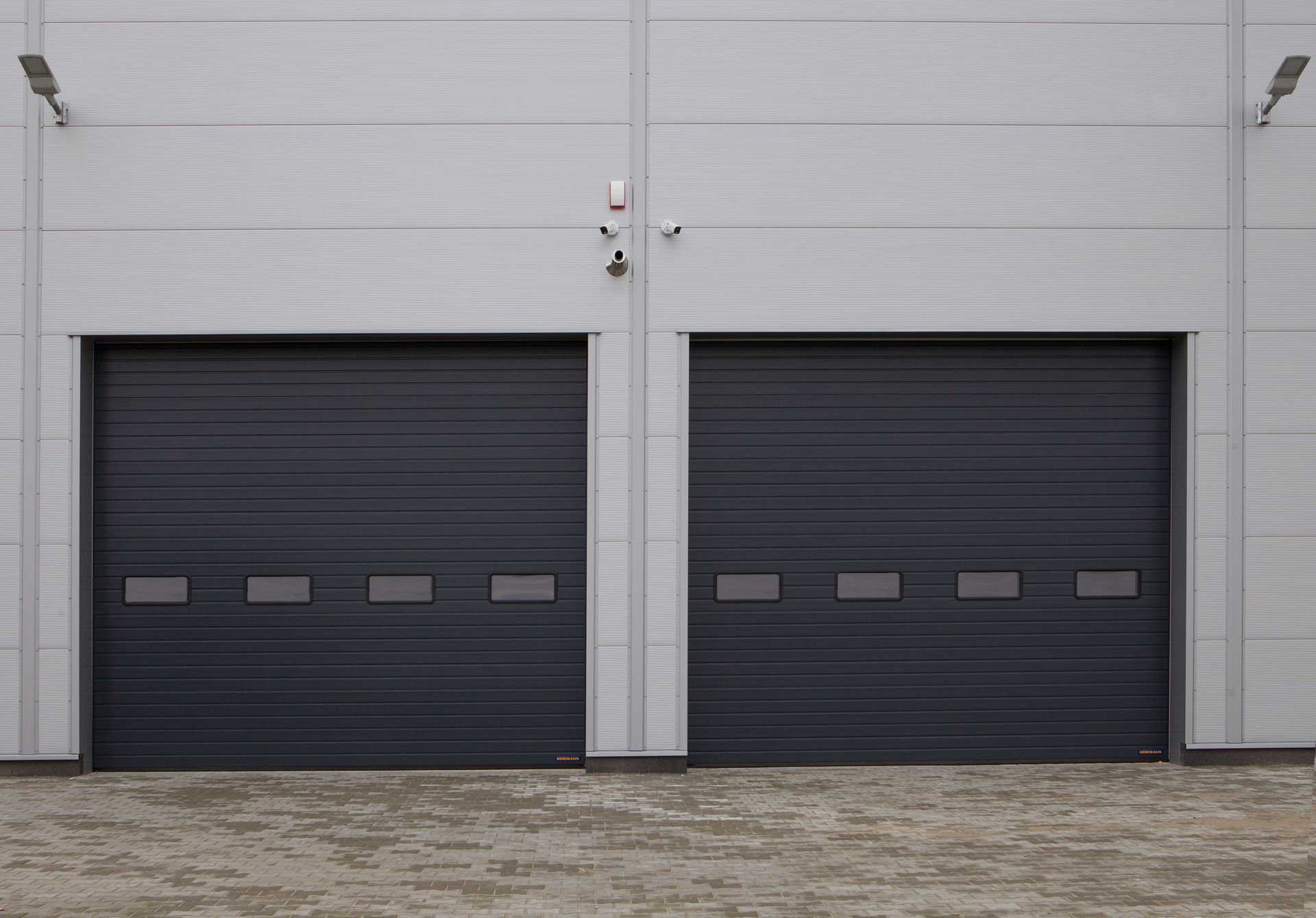 Two dark gray garage doors on a light gray industrial building
