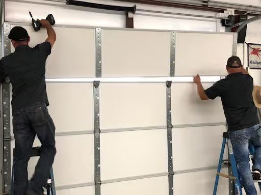 Two men installing a garage door. One uses a drill, the other aligns a panel.