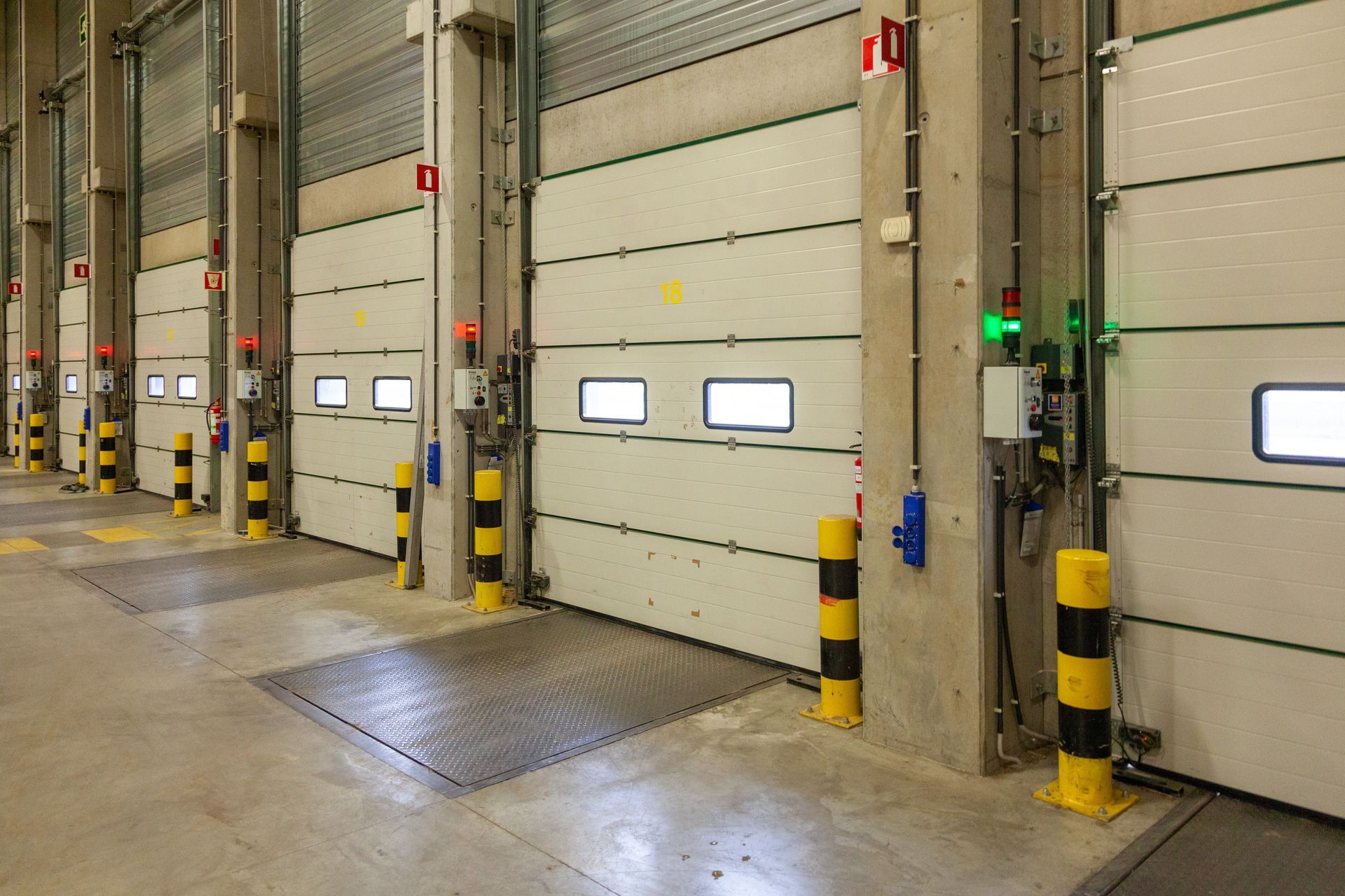 Row of industrial loading dock doors with concrete floor and safety bollards