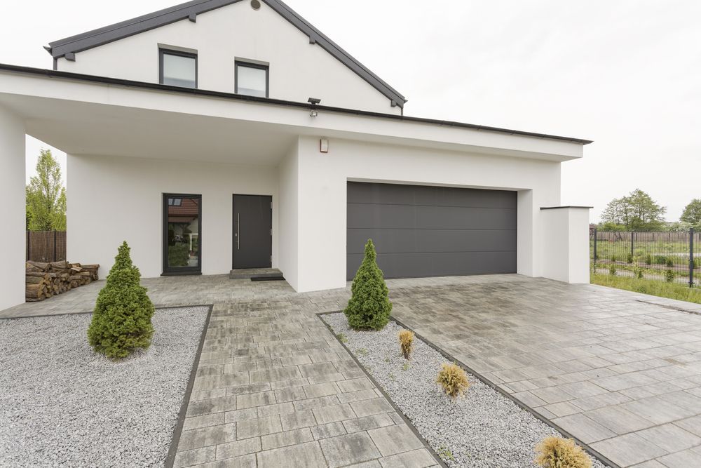 Modern White House With Gray Garage Door, Paved Driveway, and Small Trees — On The Grind In Bongaree, QLD