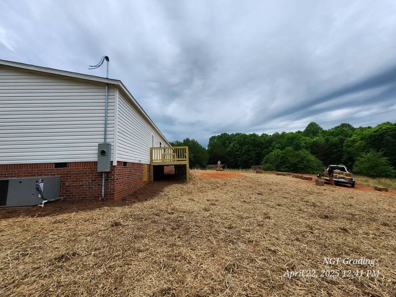 Rural backyard beside a white house with gravel ground, trees, and a parked utility vehicle under cloudy sky