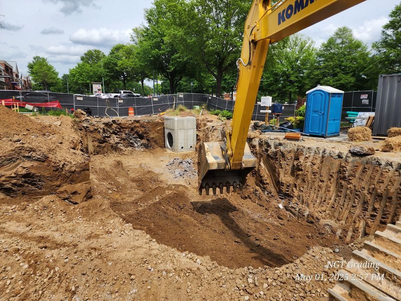 Excavator digging a large trench at a construction site with dirt piles and a blue portable toilet.