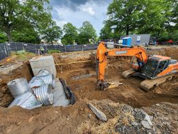 Orange excavator digging a dirt trench at a construction site with sandbags and concrete blocks nearby