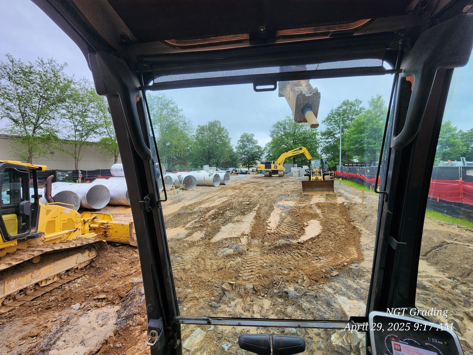 View from a construction vehicle cab over a muddy roadwork site with excavator and trucks ahead