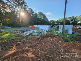 Rural yard with damaged structures, debris piles, and an orange tank at sunset