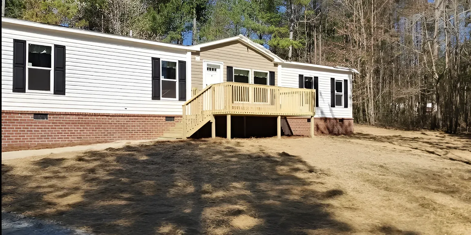 Single-story white house with brick base and wooden front deck on a wooded hillside