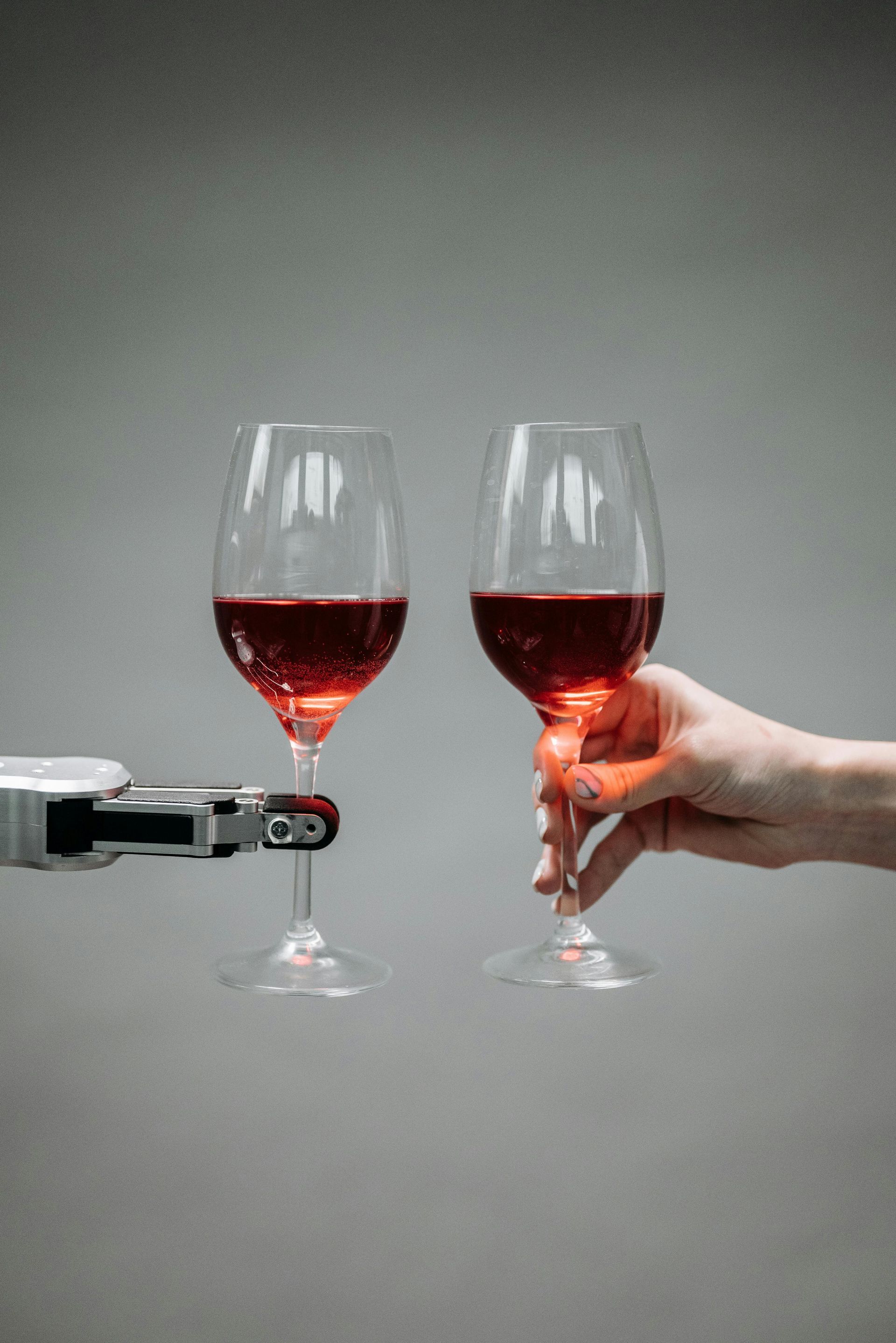 Uma pessoa segura duas taças de vinho ao lado de um braço robótico.