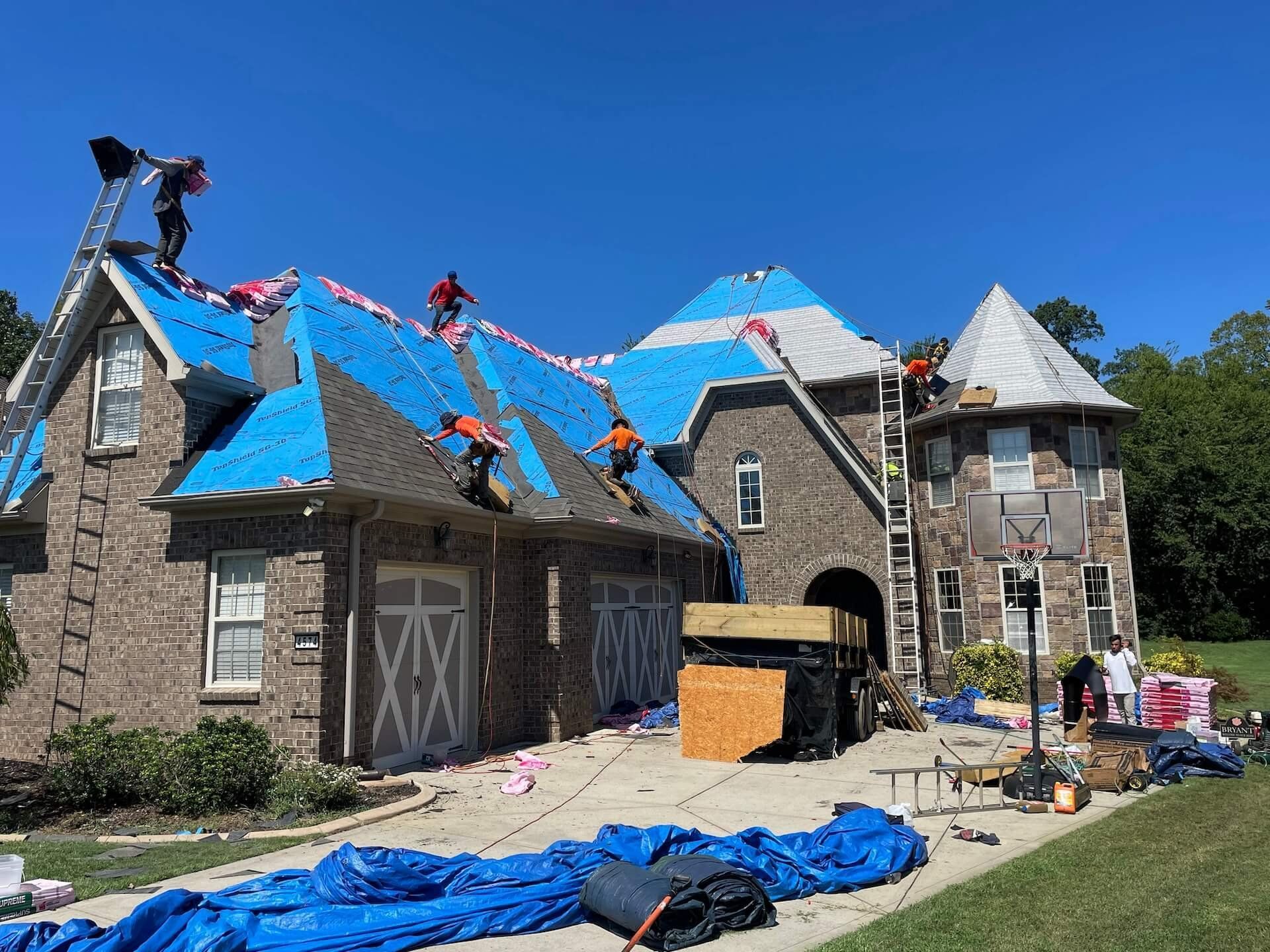 A group of people are working on the roof of a large brick house.