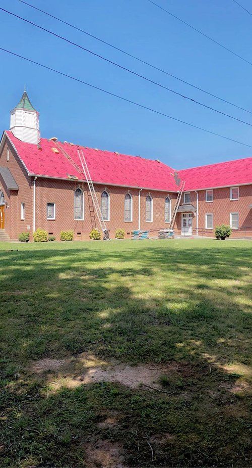 A large brick church with a red roof is sitting in the middle of a grassy field.