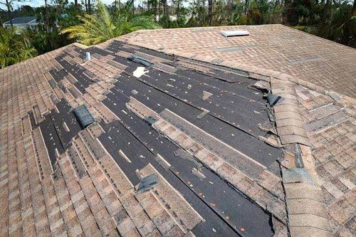 A roof with a lot of shingles missing and a skylight.