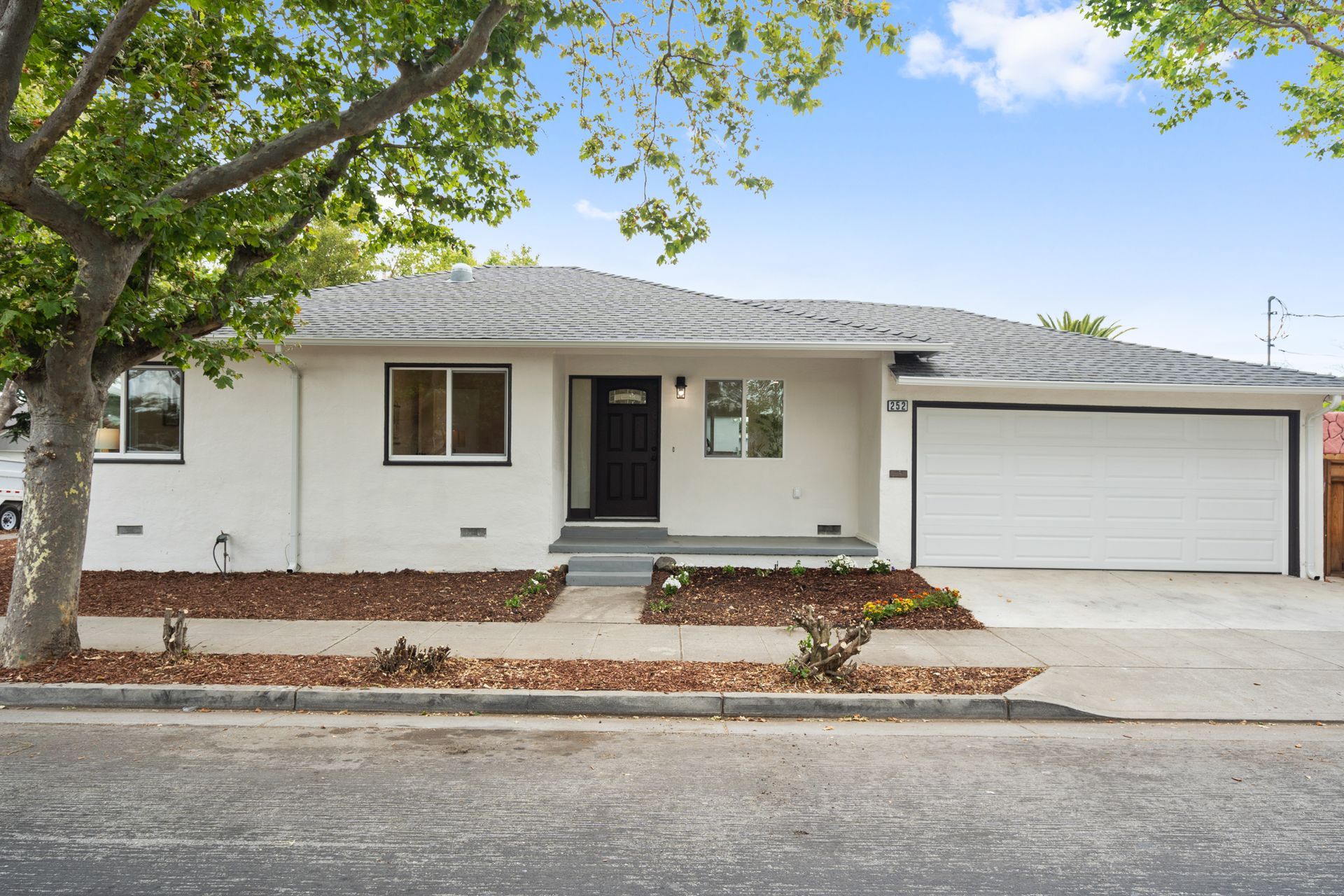 A white house with a garage and a tree in front of it