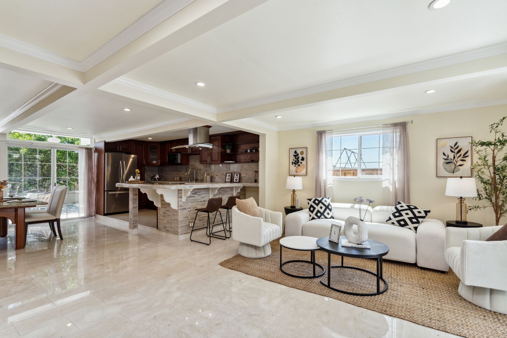 A living room with a couch , chairs , tables and a kitchen.