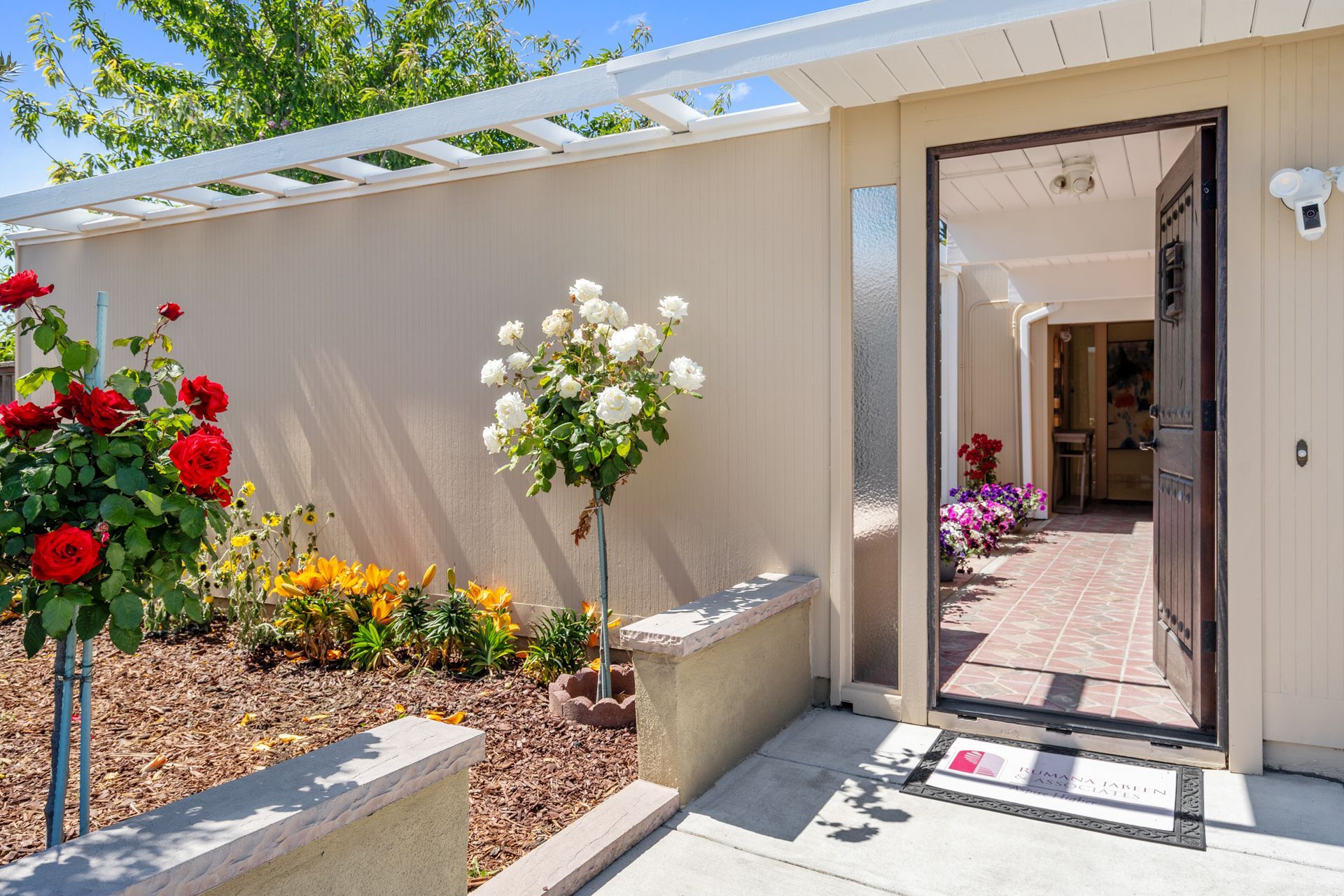 The front door of a house is open and surrounded by flowers.