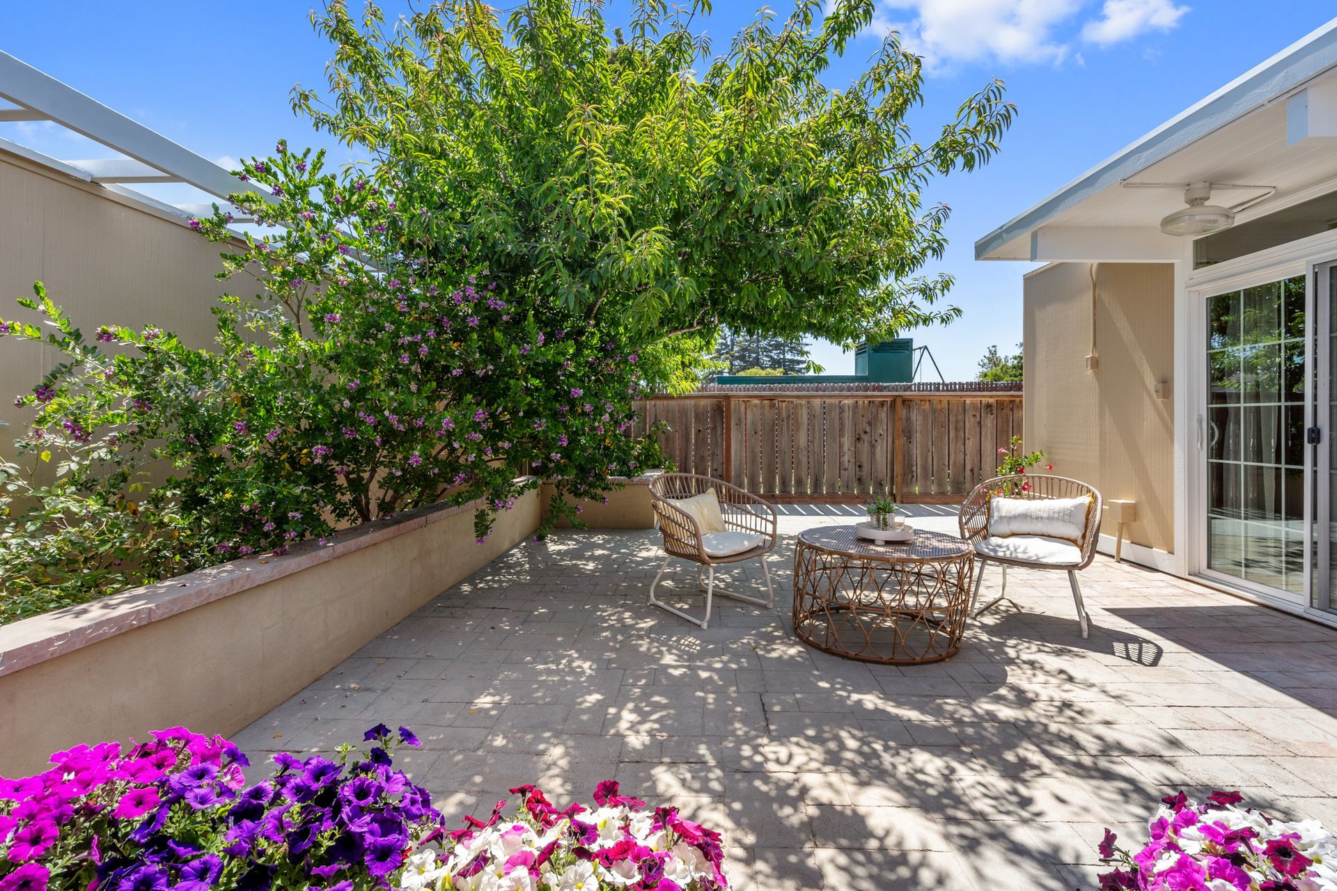 A patio with a table , chairs and flowers in front of a house.