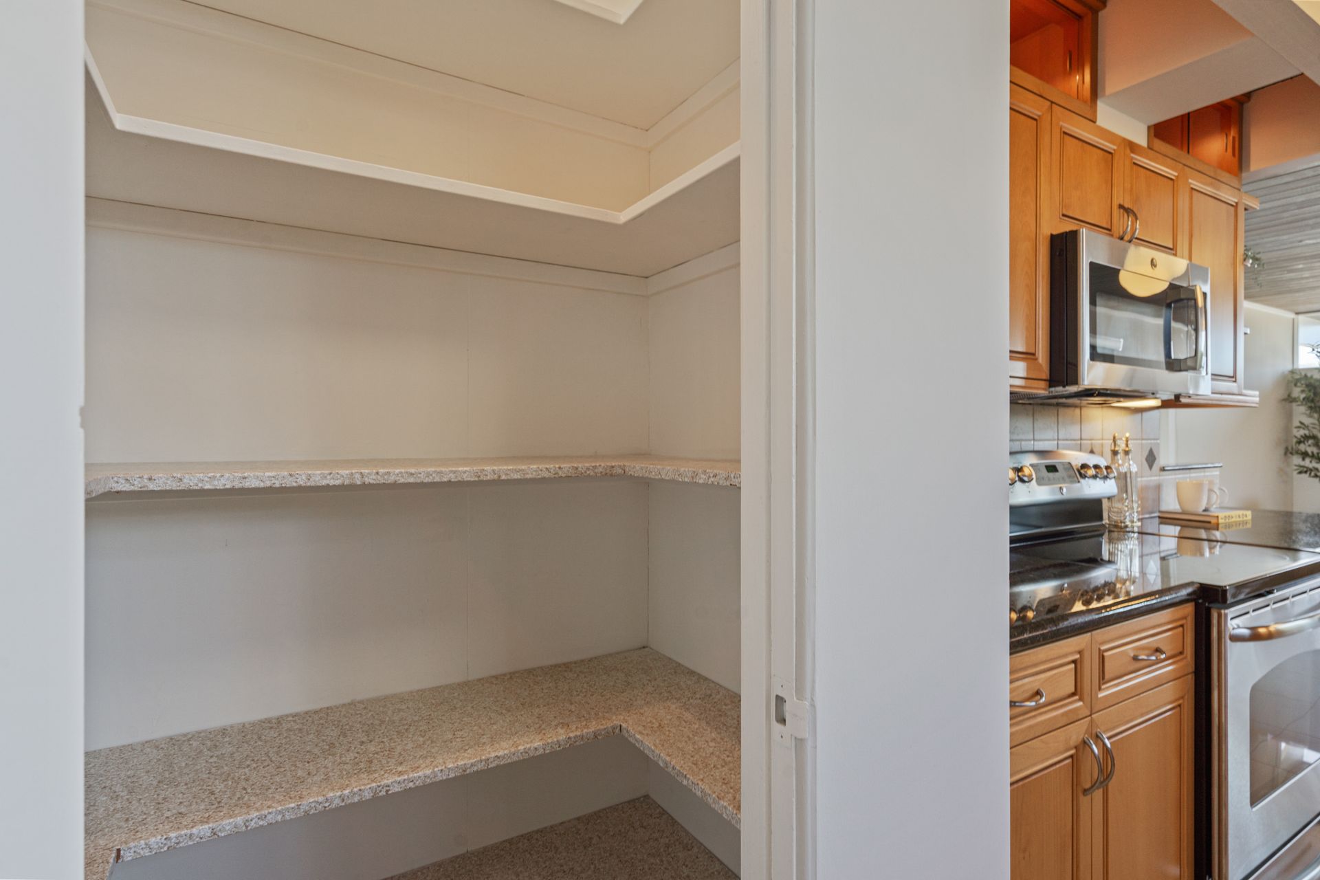 A pantry in a kitchen next to a stove and microwave.