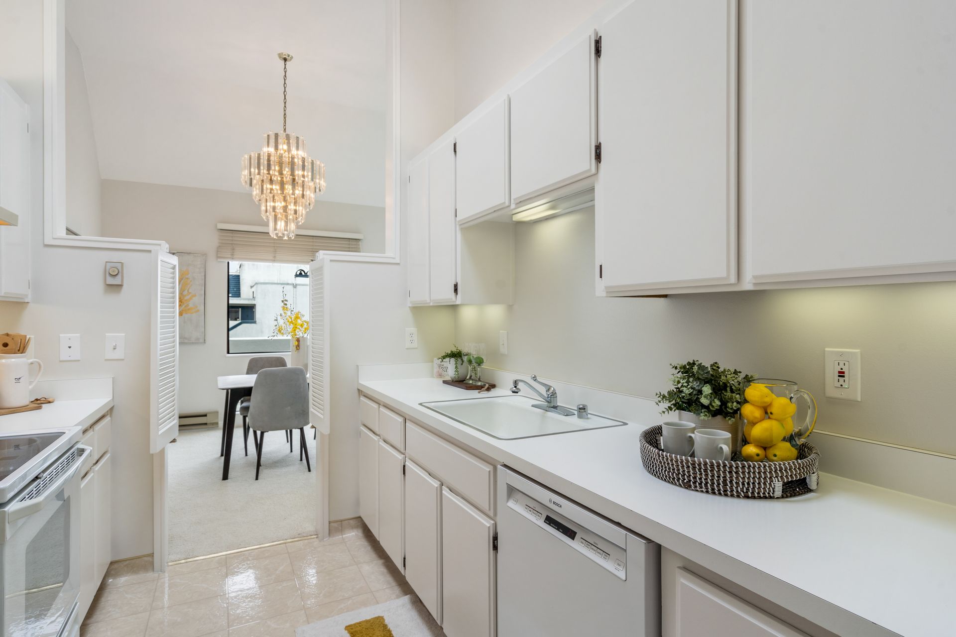 A kitchen with white cabinets , a sink , a dishwasher , a stove , and a chandelier.