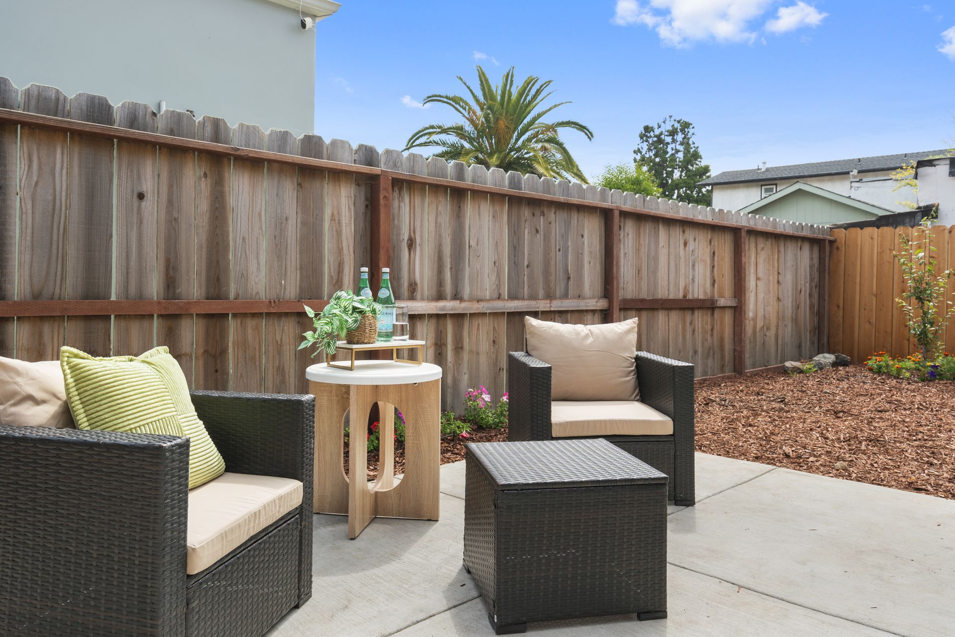 A patio with chairs and a table in front of a wooden fence.