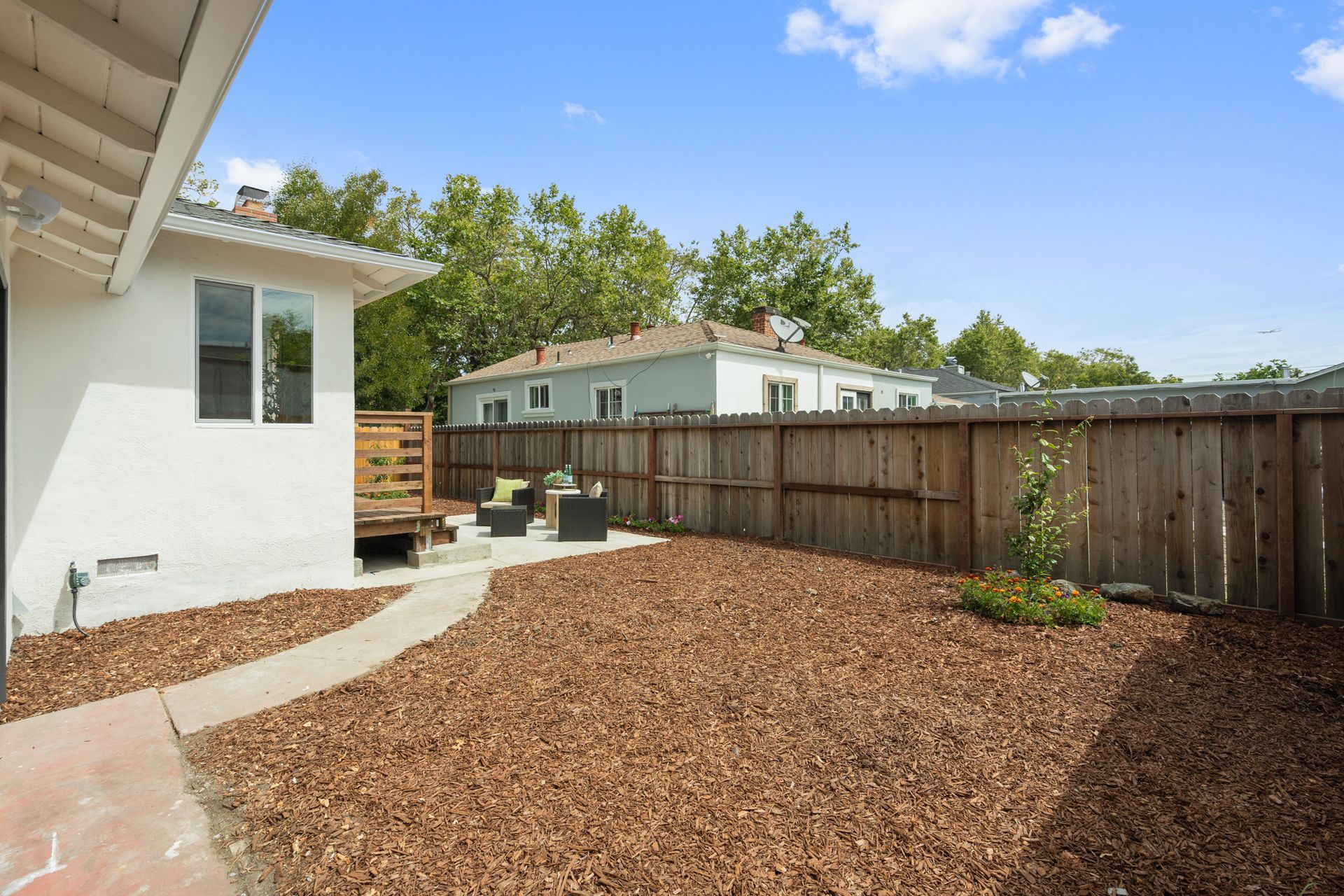 The backyard of a house with a wooden fence and mulch.