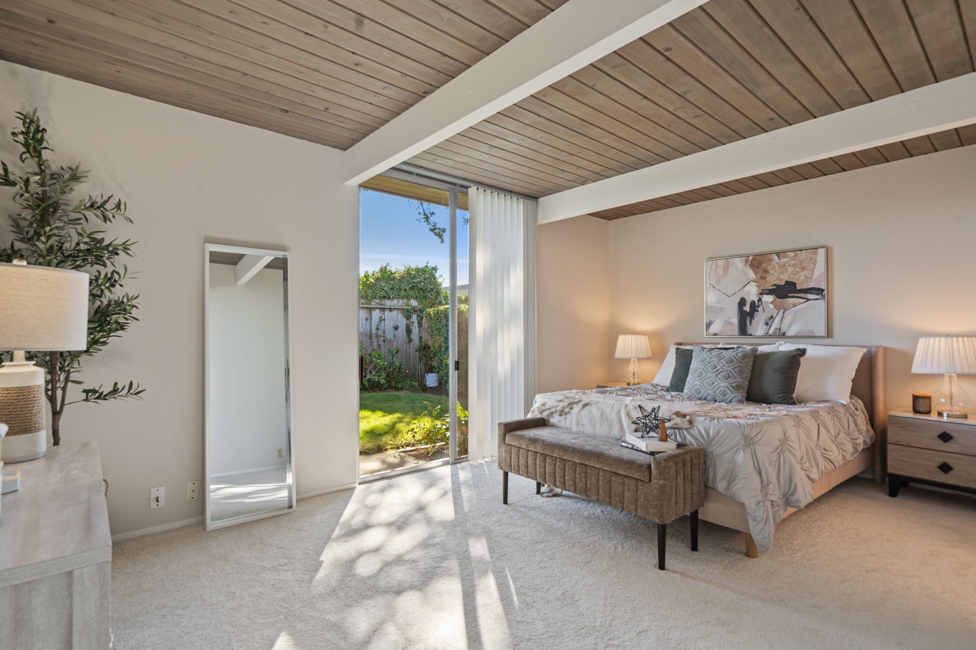 A bedroom with a large bed , a bench , a mirror and a sliding glass door.
