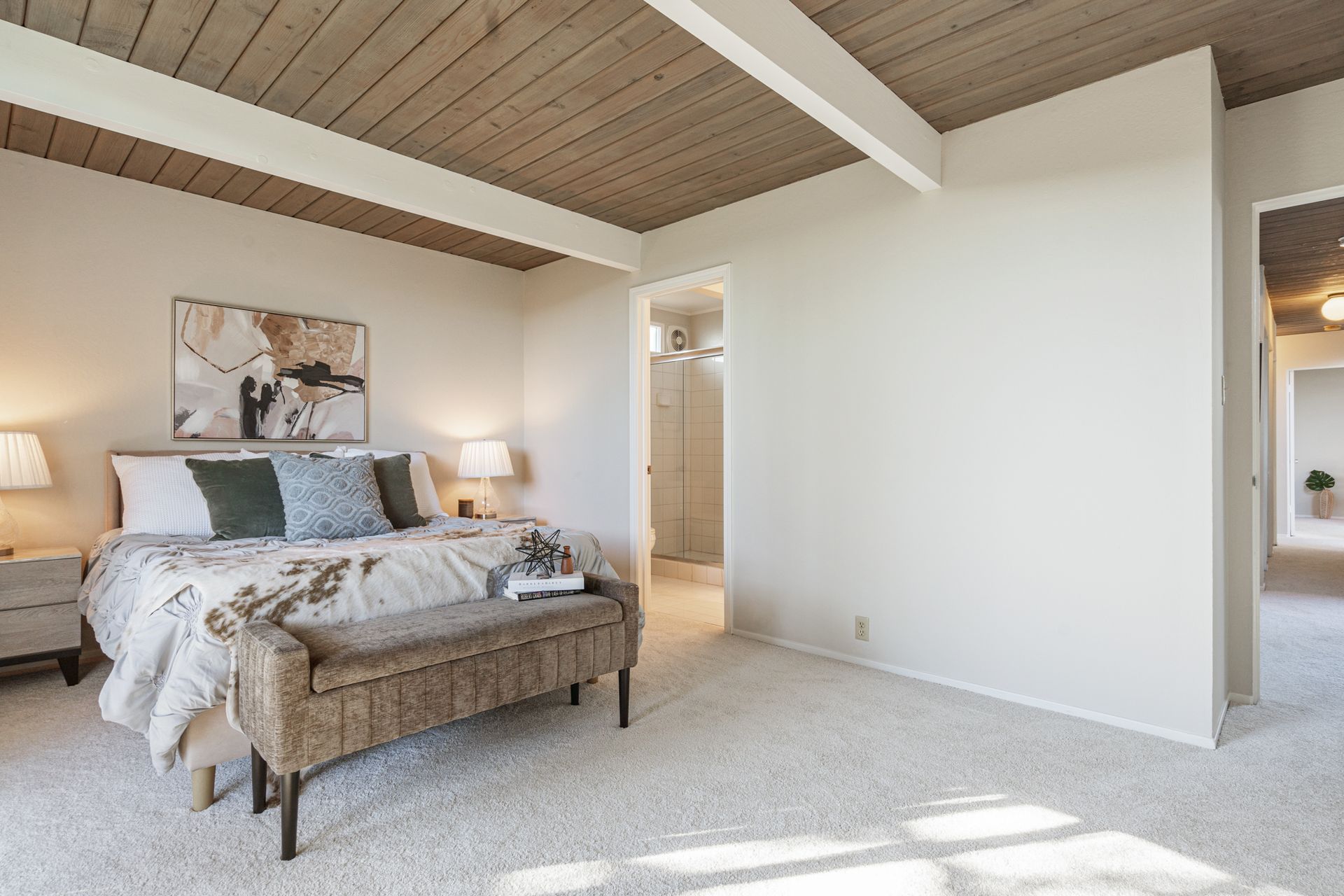A bedroom with a bed , bench , lamps and a wooden ceiling.