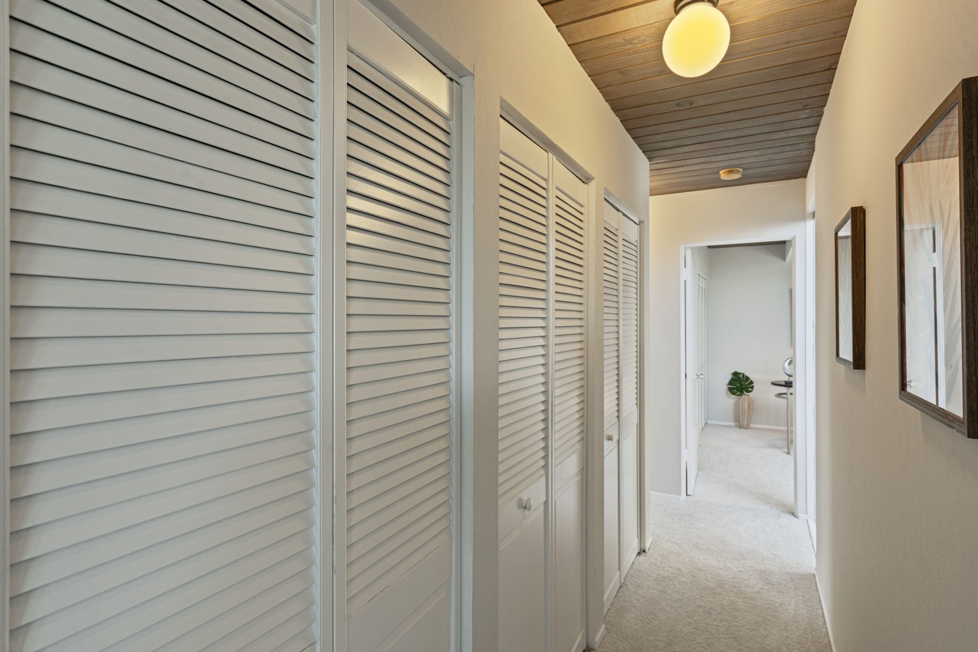 A hallway with white shutters on the doors and a light on the ceiling.