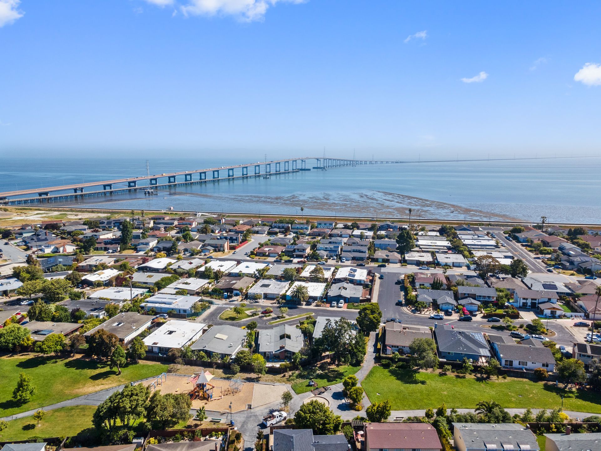 An aerial view of a residential area next to the ocean with a bridge in the background.