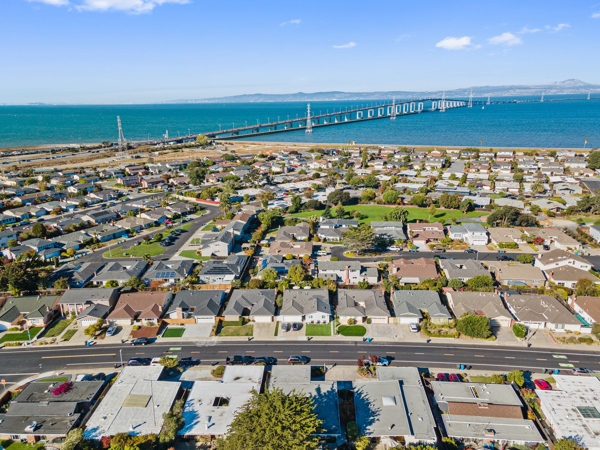 An aerial view of a residential area next to the ocean with a bridge in the background.