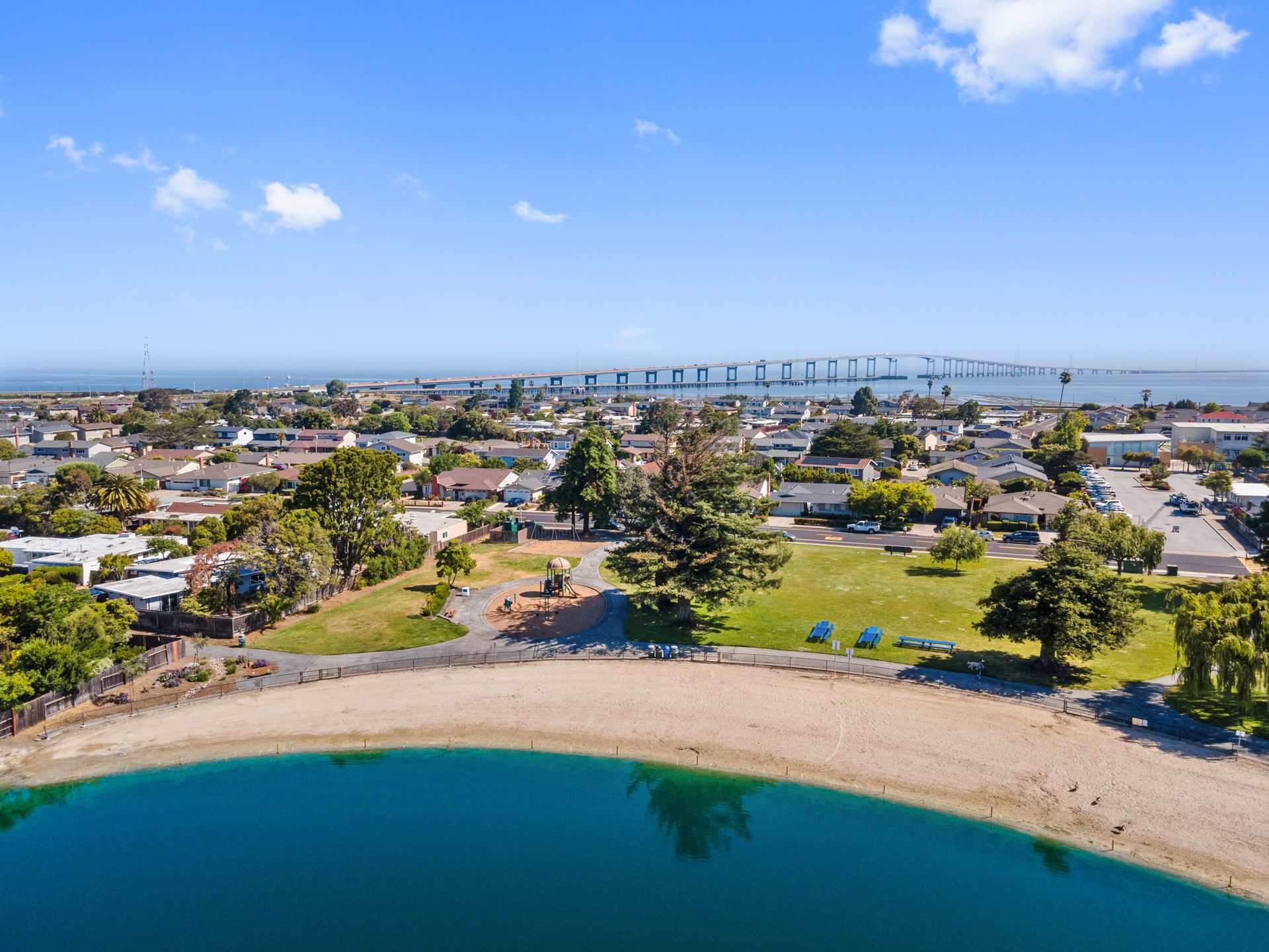 An aerial view of a beach and a lake with a bridge in the background.