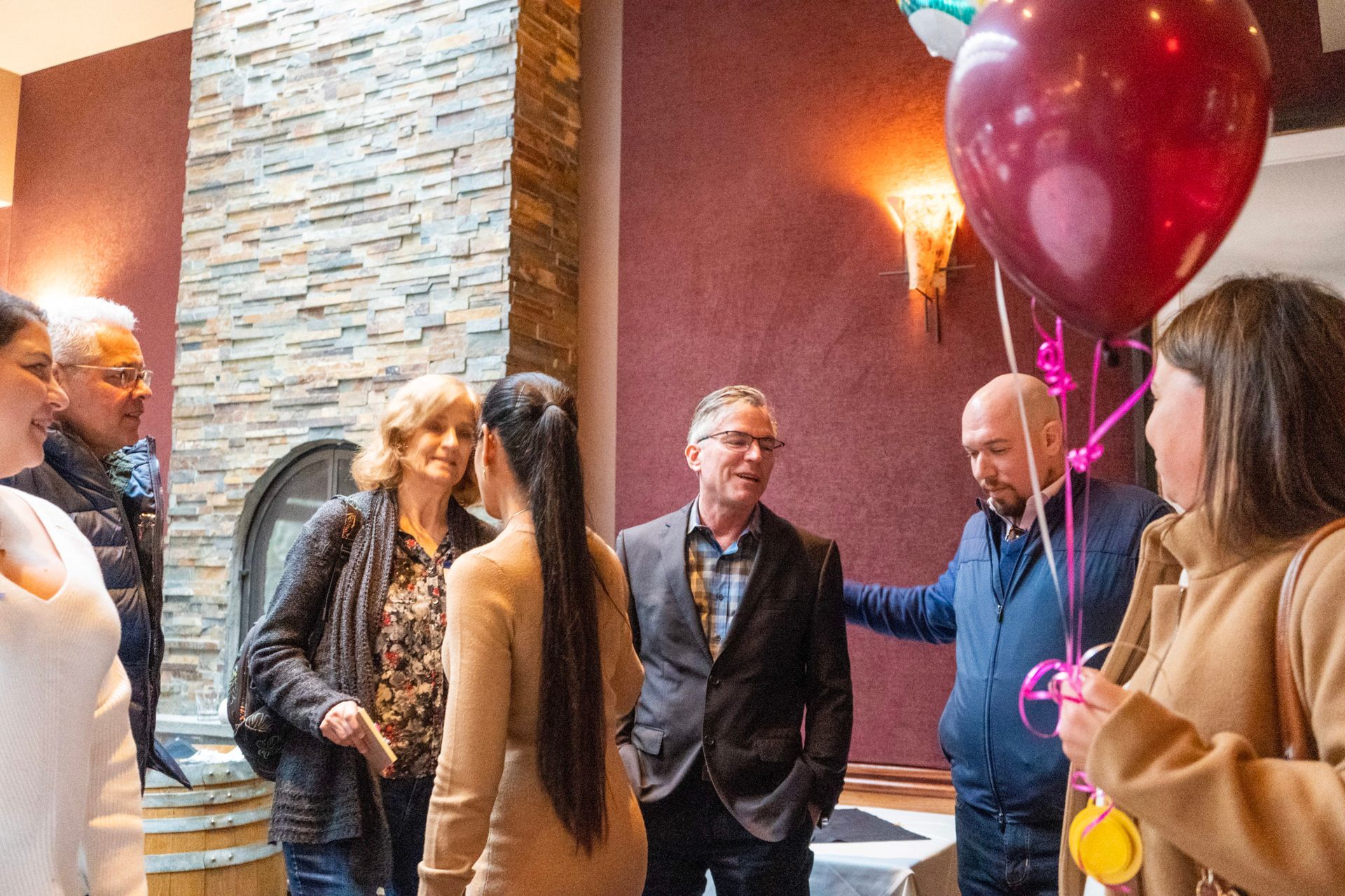 A group of people are standing in a room with balloons and talking to each other.