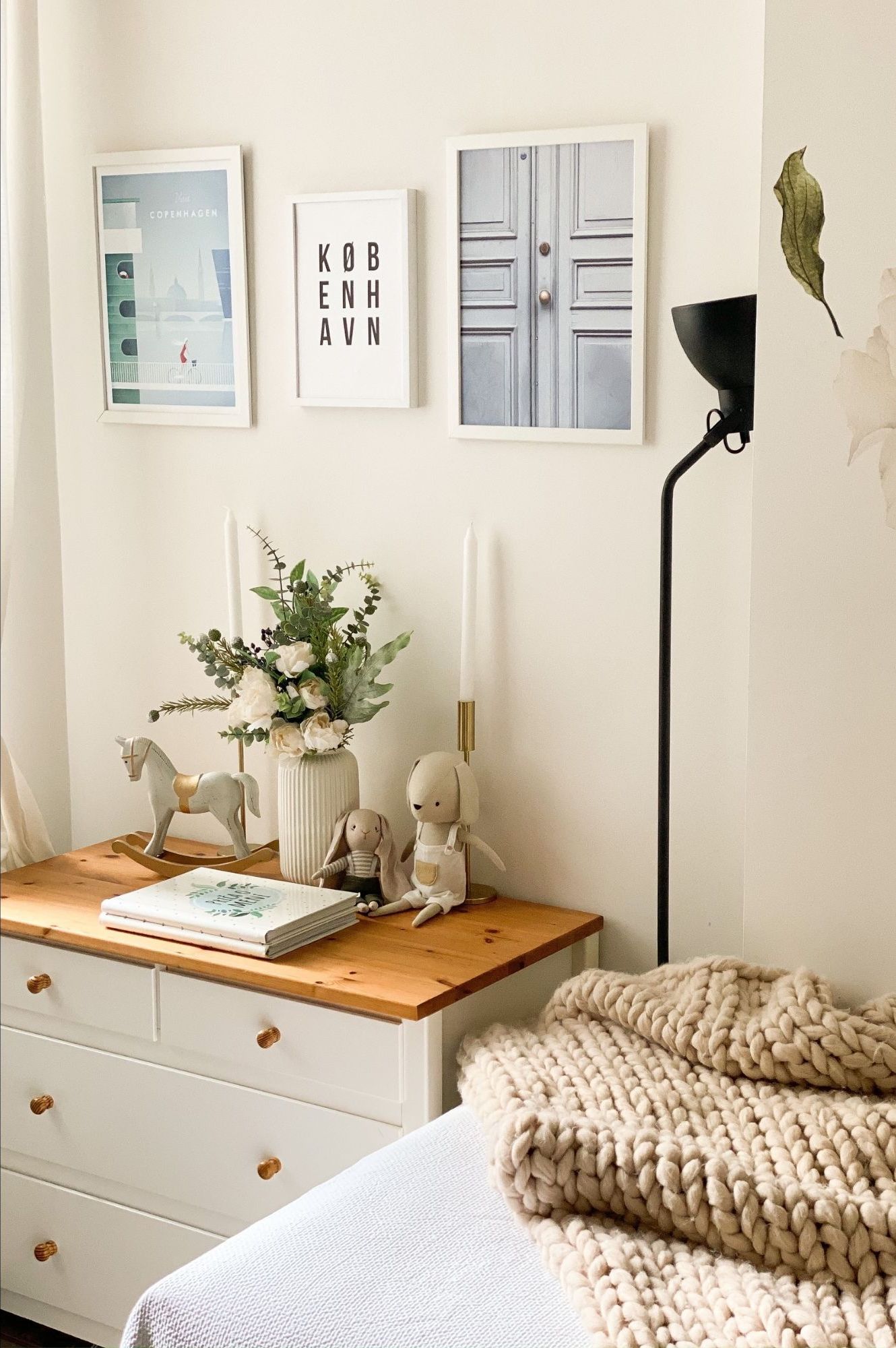 A bedroom with a bed , dresser , lamp and pictures on the wall.