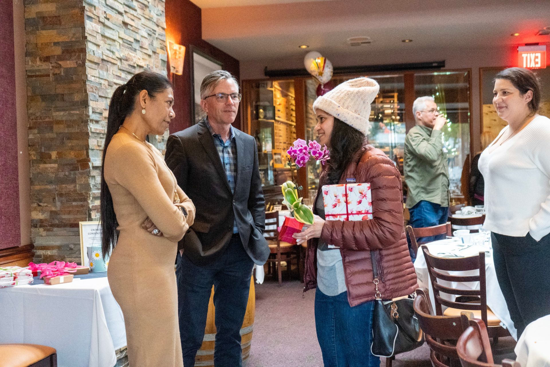 A group of people are standing around a table in a restaurant talking to each other.