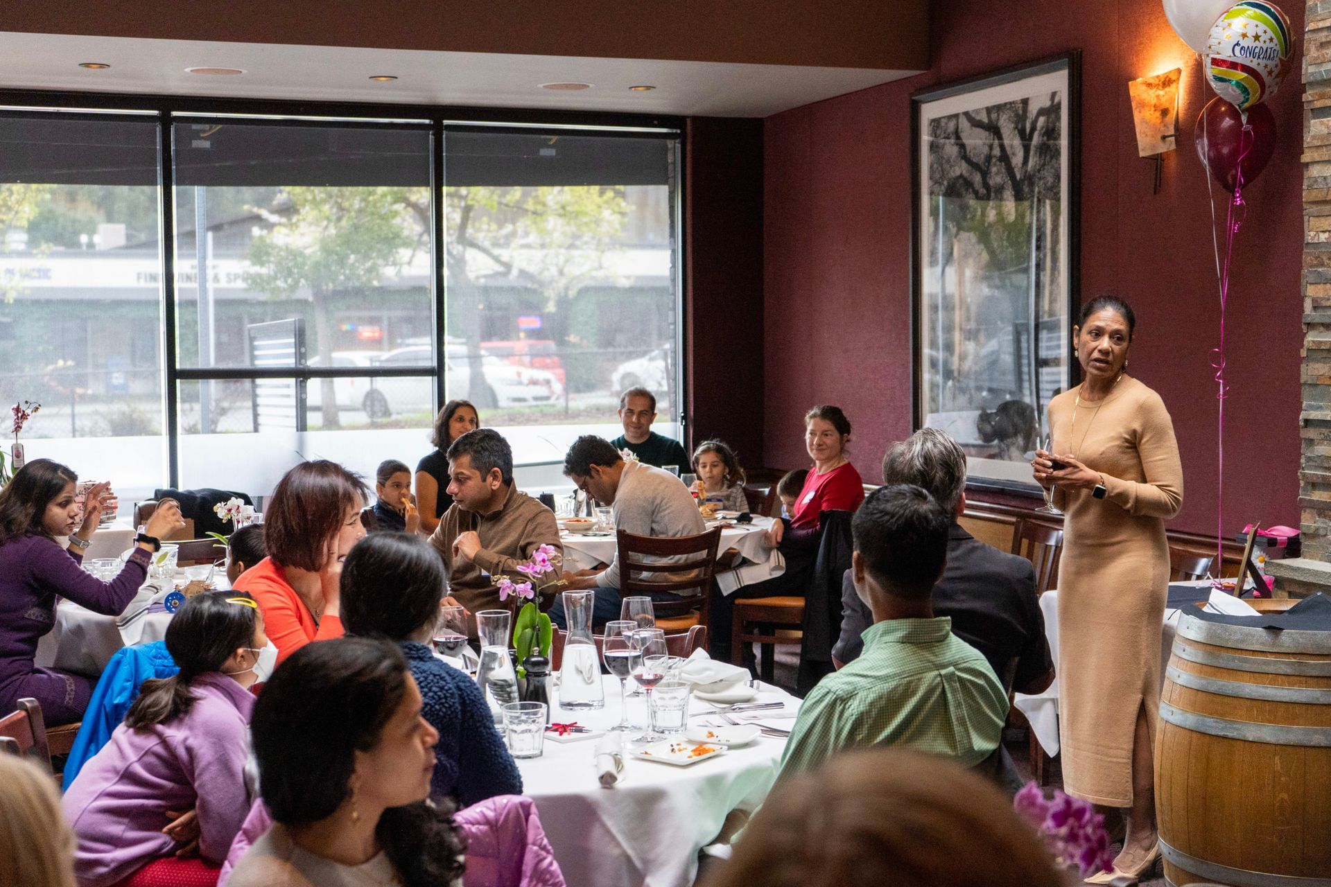 A woman is standing in front of a group of people sitting at tables in a restaurant.