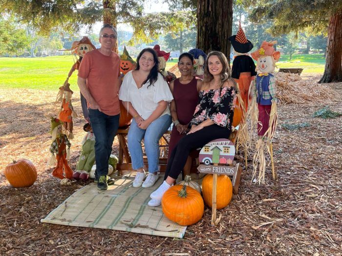 A group of people are posing for a picture in a park with pumpkins and scarecrows.