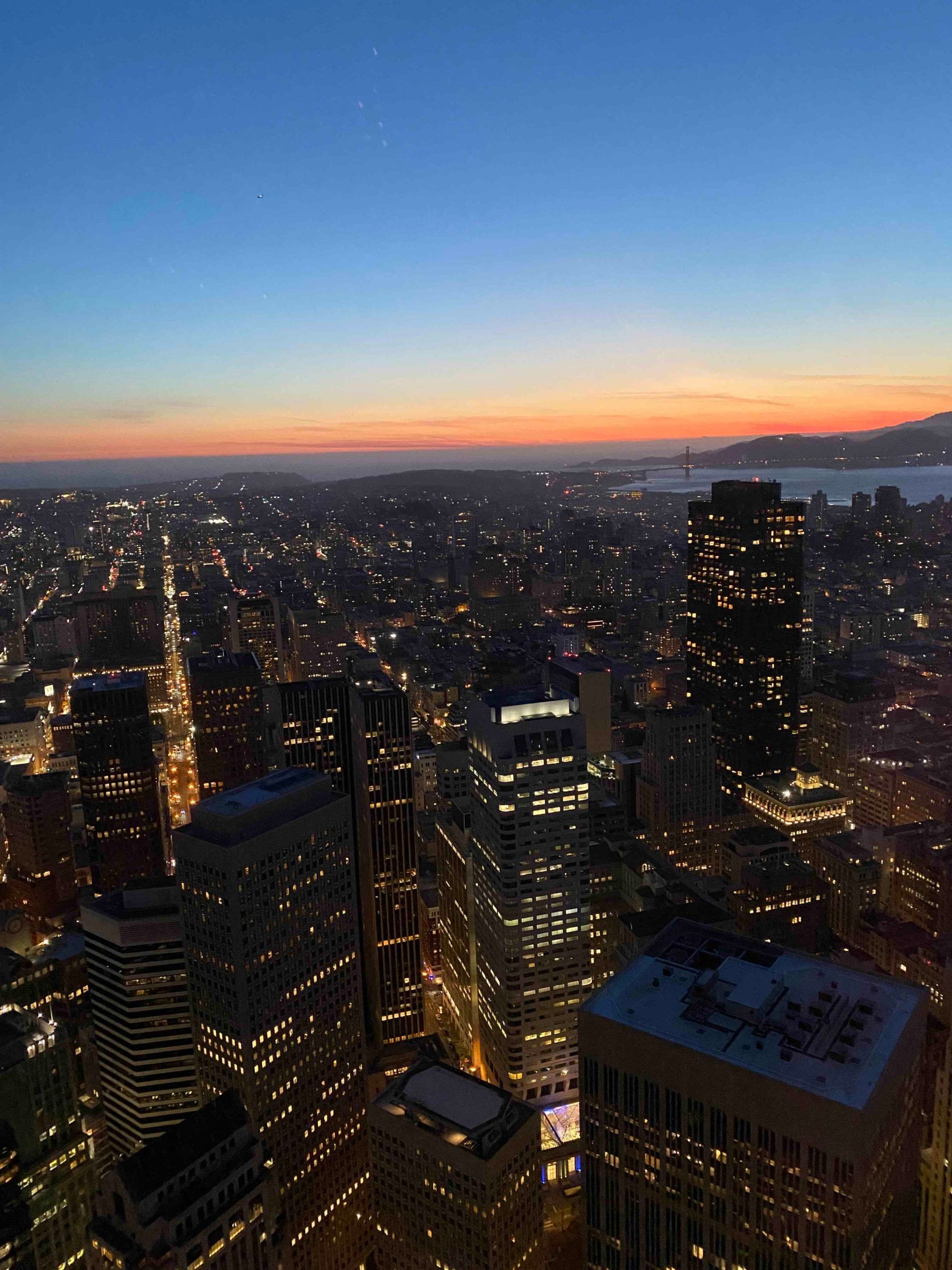 An aerial view of a city at night with a sunset in the background