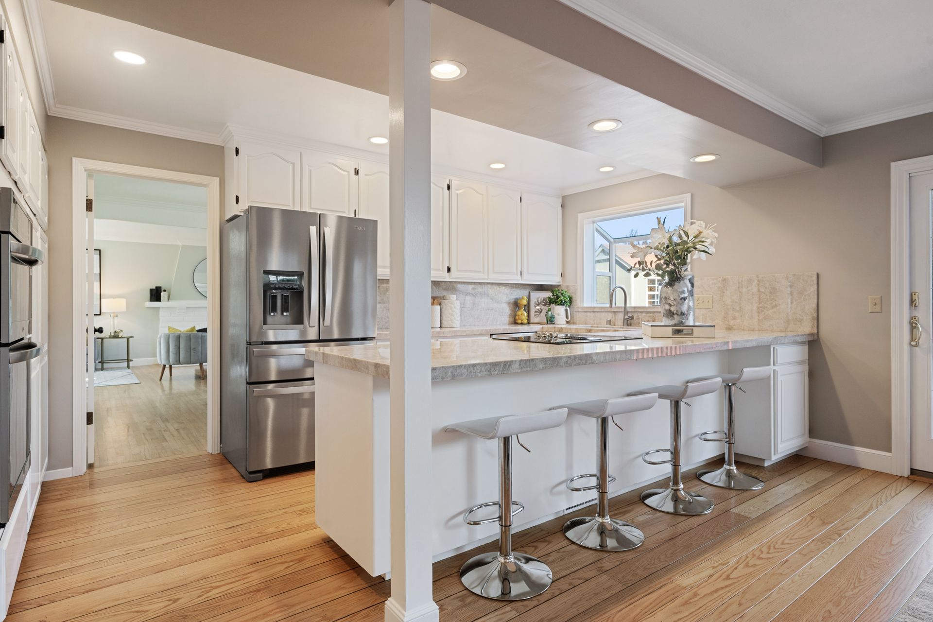 A kitchen with white cabinets , stainless steel appliances , a refrigerator and a bar.