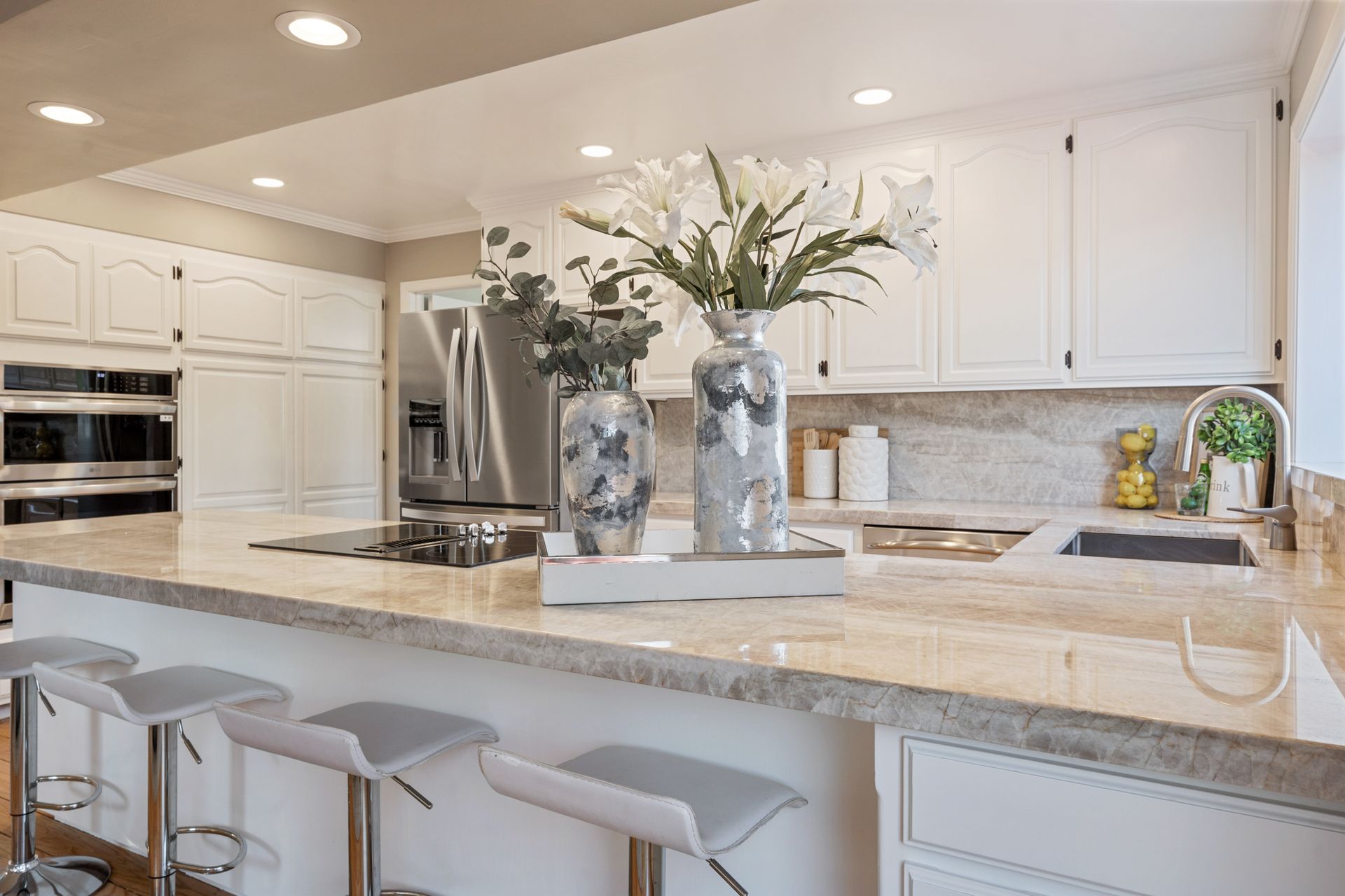 A kitchen with white cabinets , granite counter tops , stools and a refrigerator.