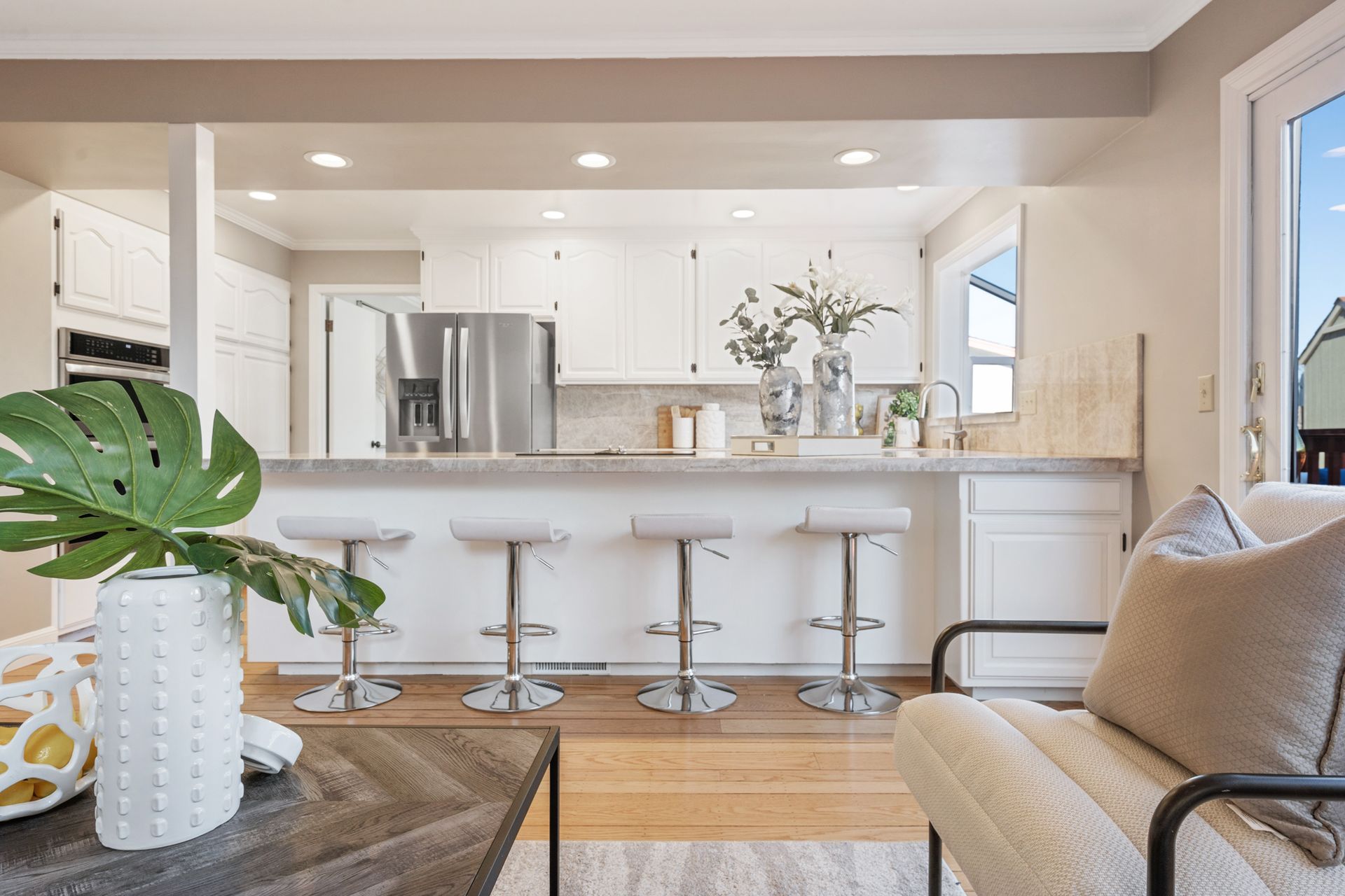 A living room with a chair , table , and kitchen in the background.