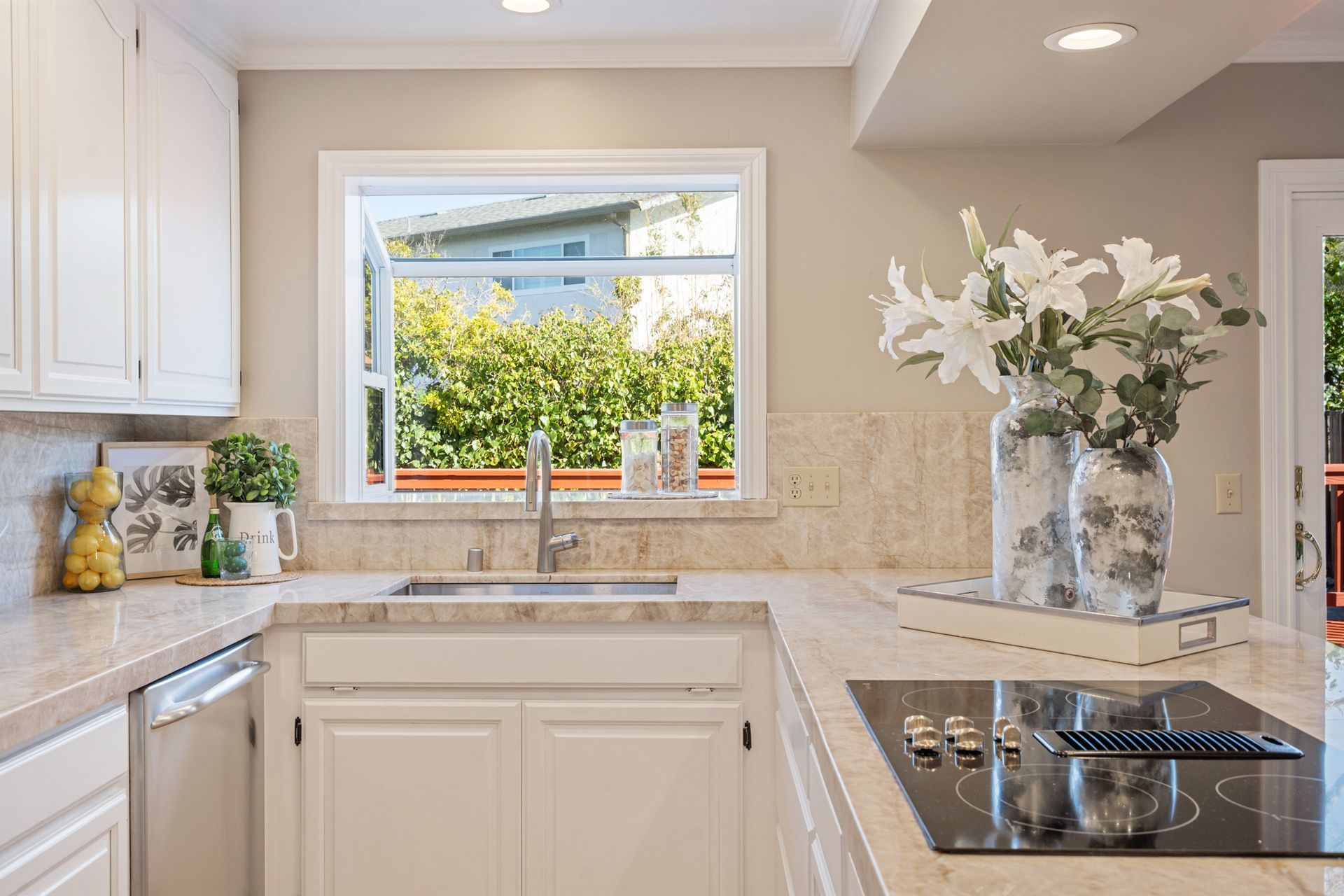 A kitchen with white cabinets , a sink , a stove top oven , and a window.
