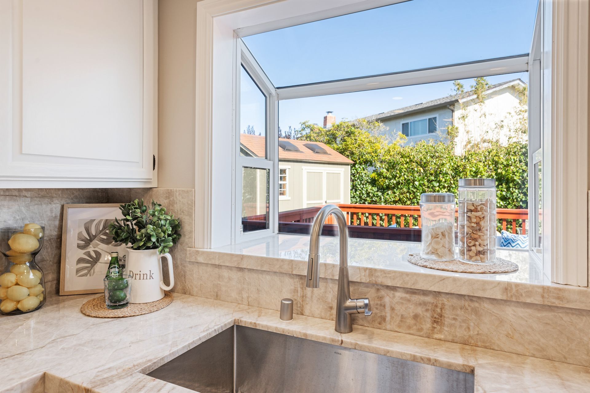 A kitchen with a sink and a window with a view of a house.
