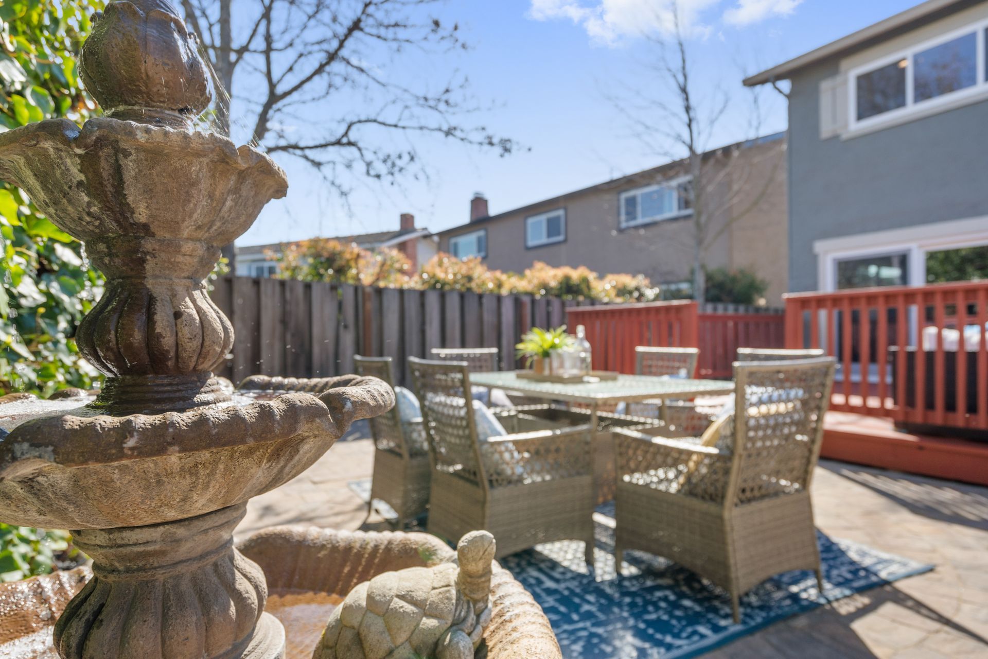 A patio with a table and chairs and a fountain in the backyard.