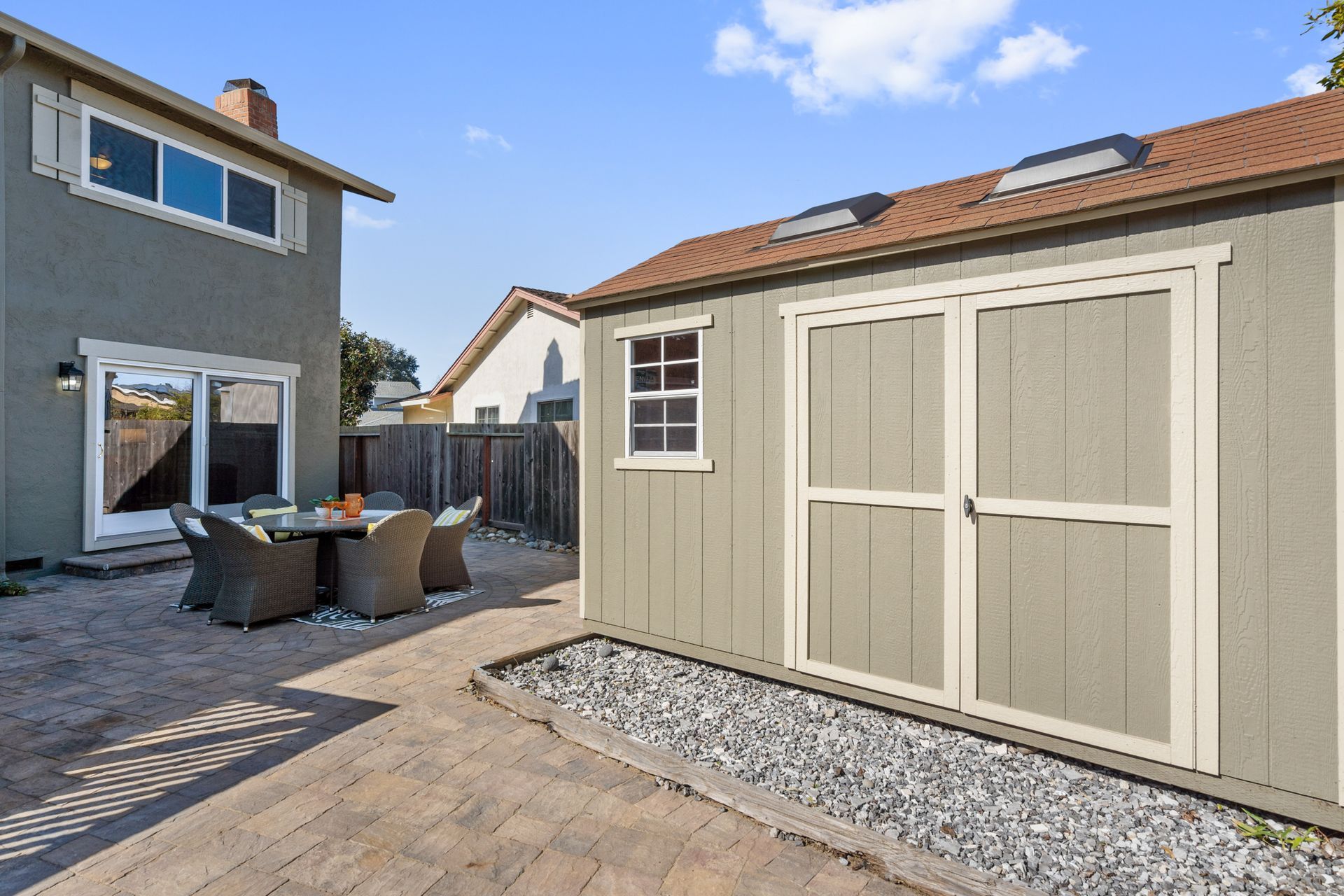 A shed in a backyard next to a house with a table and chairs.