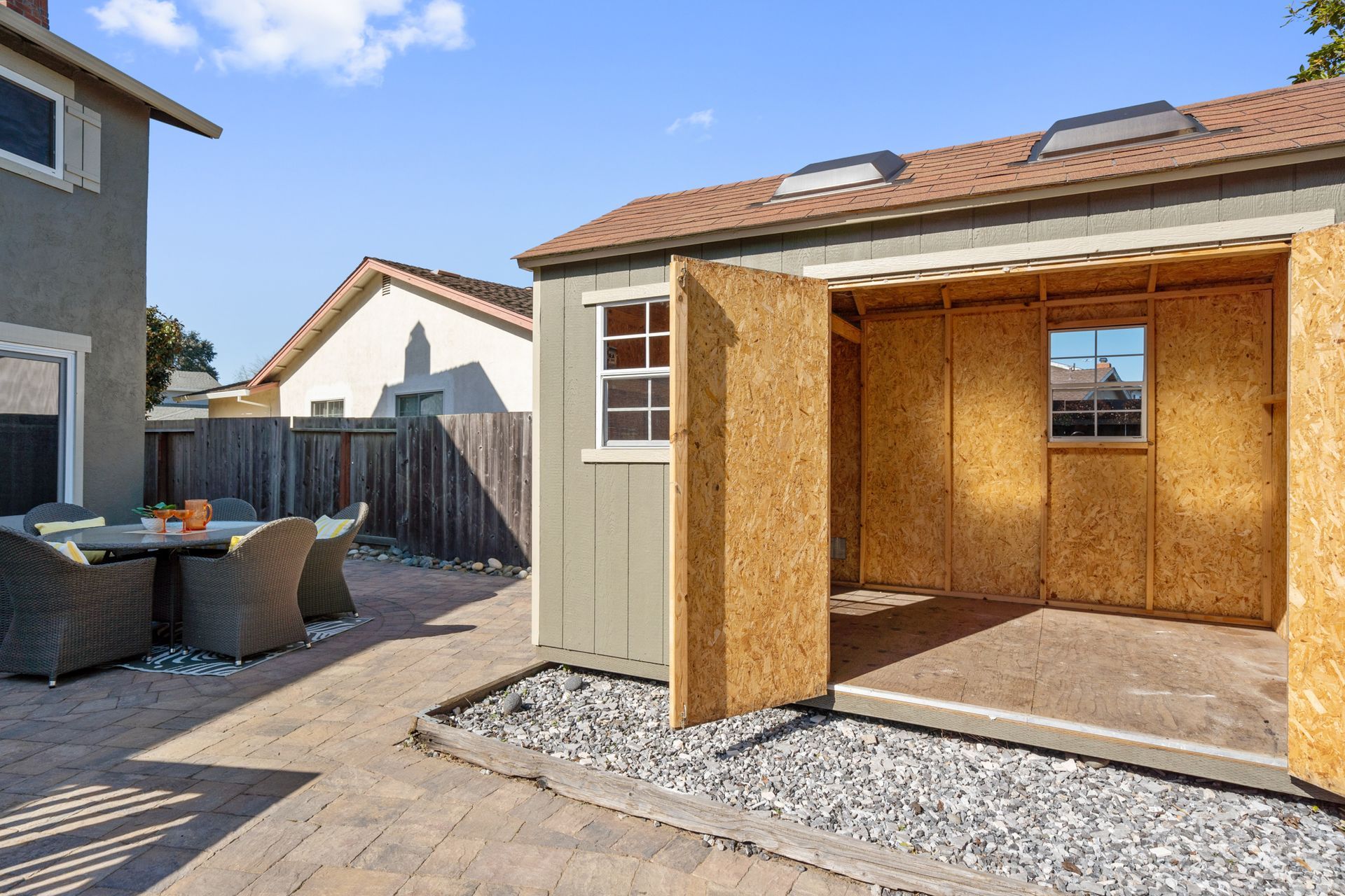 A shed with its doors open in a backyard next to a house.