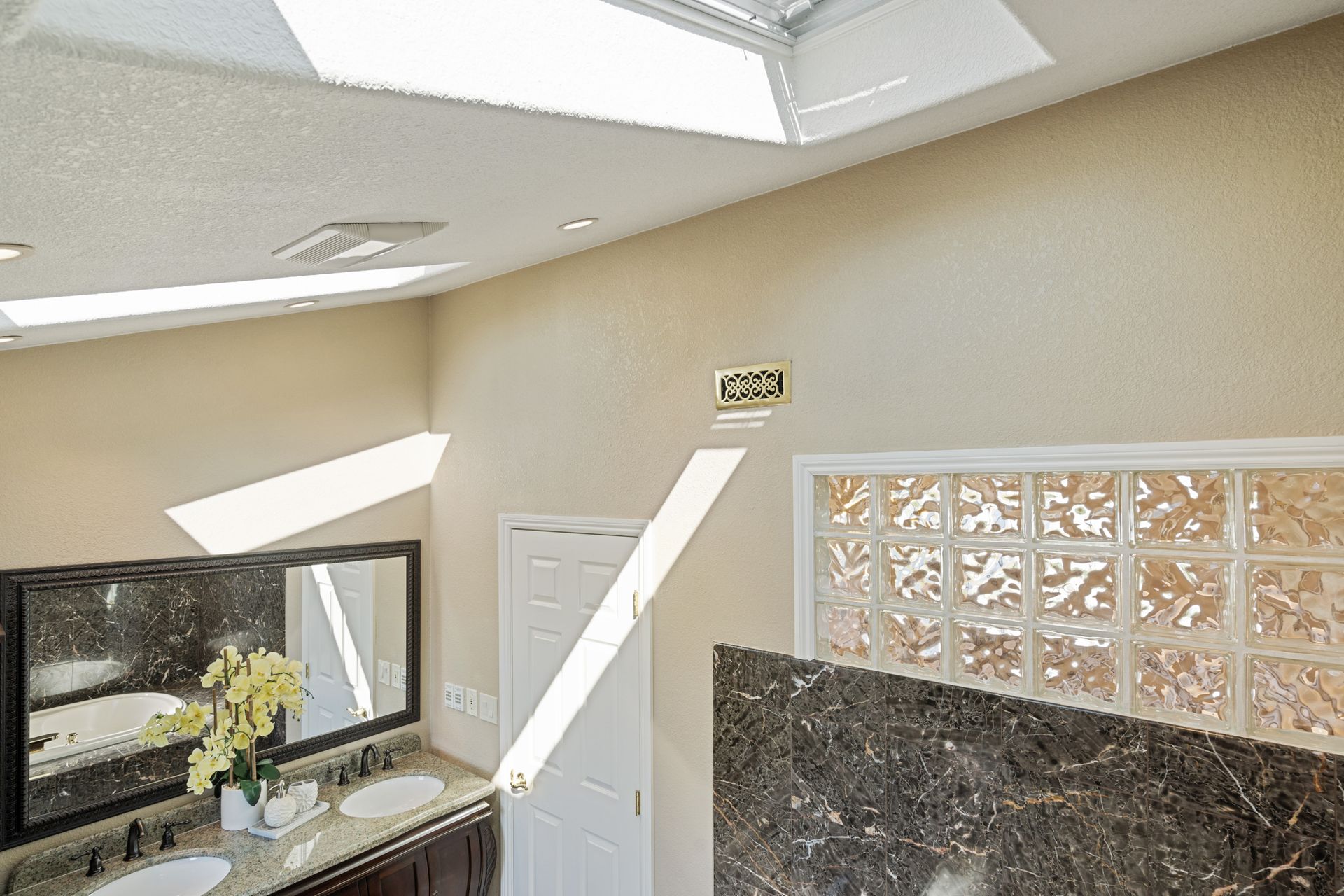A bathroom with two sinks , a mirror and a skylight.