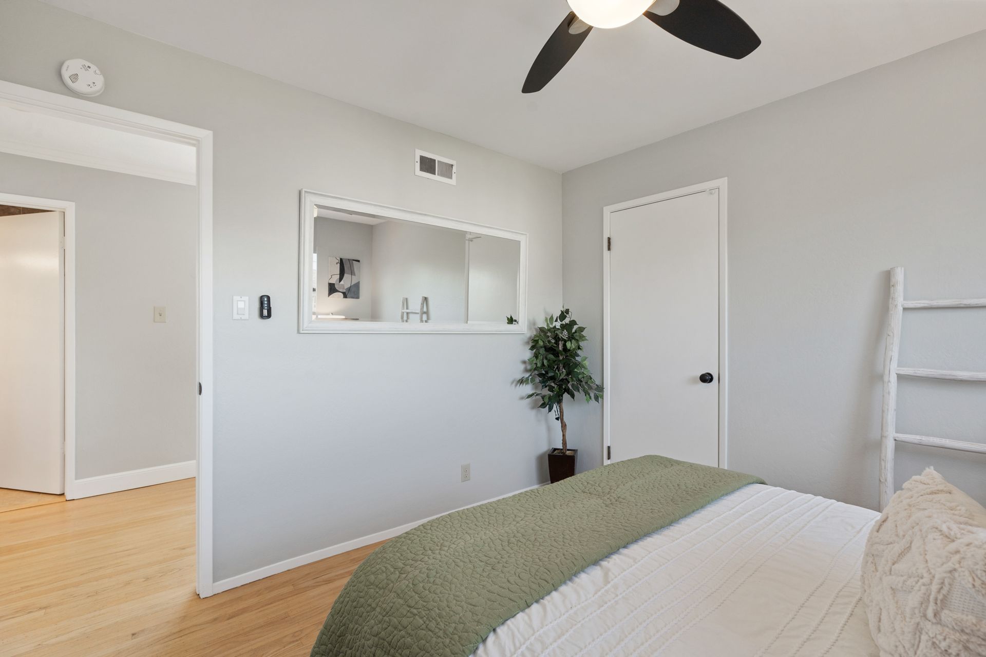 A bedroom with a bed , ceiling fan , mirror and ladder.