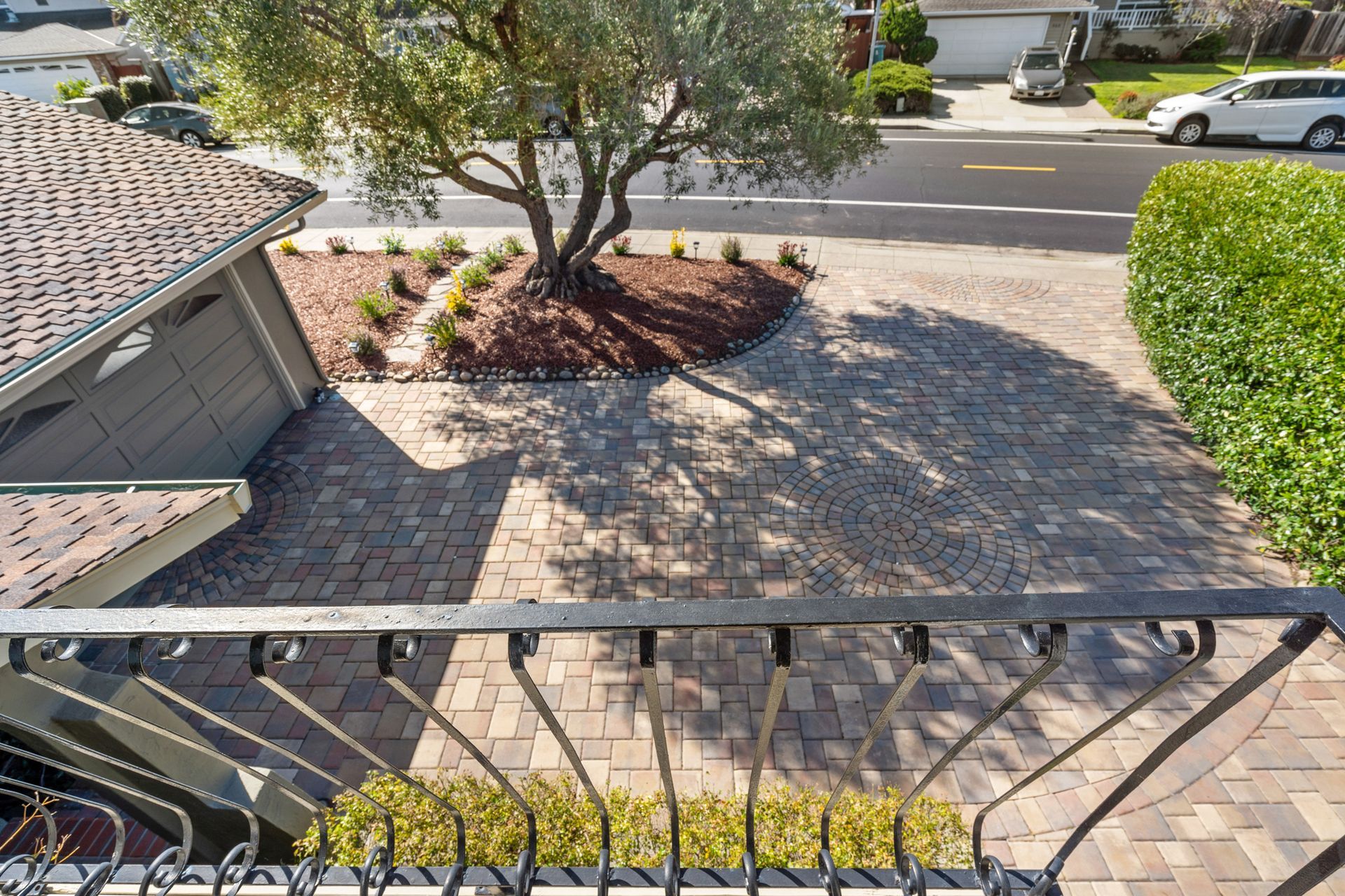 A balcony overlooking a brick driveway with a tree in the middle of it.