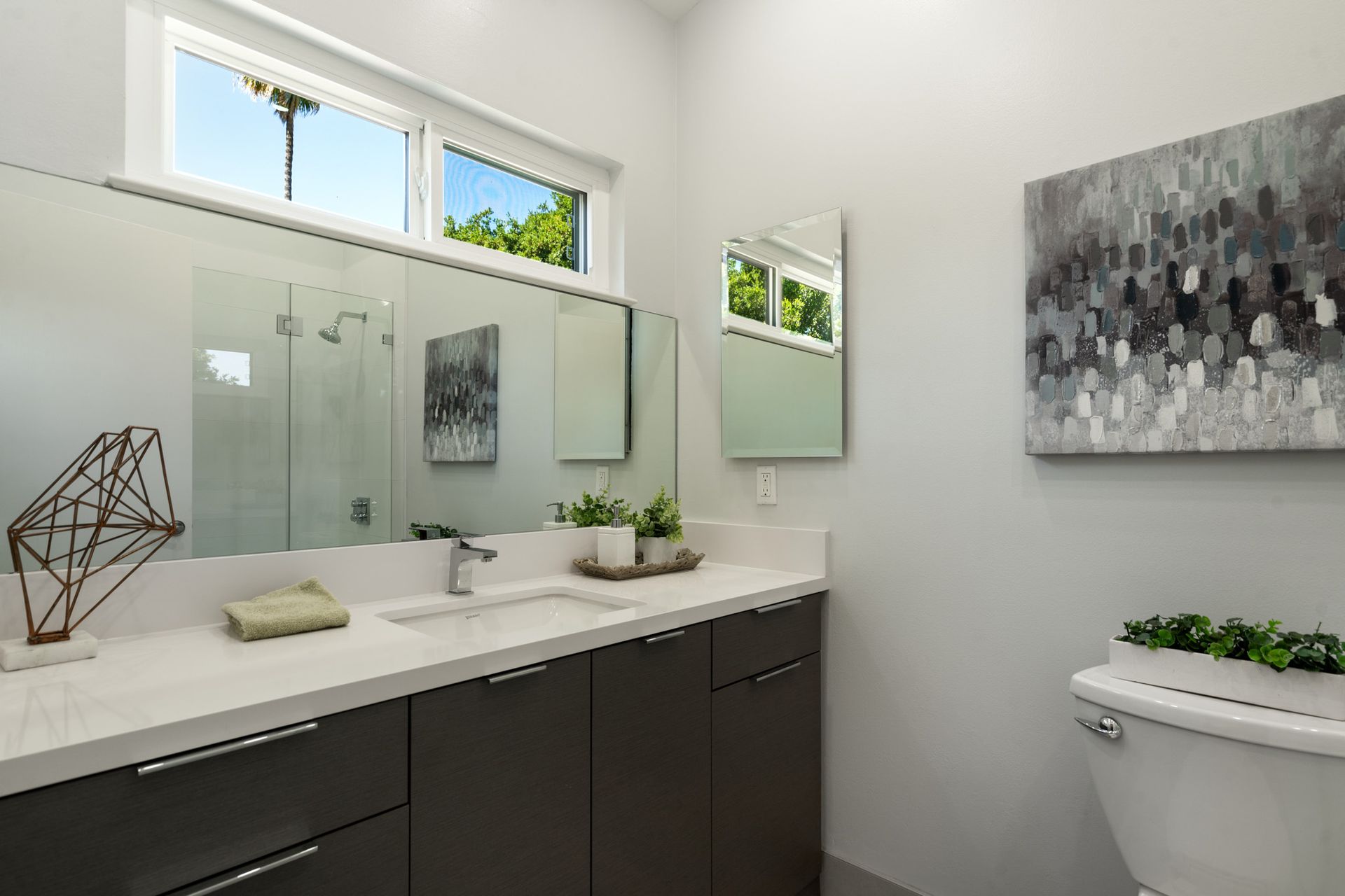 A bathroom with a sink , toilet , mirror and window.