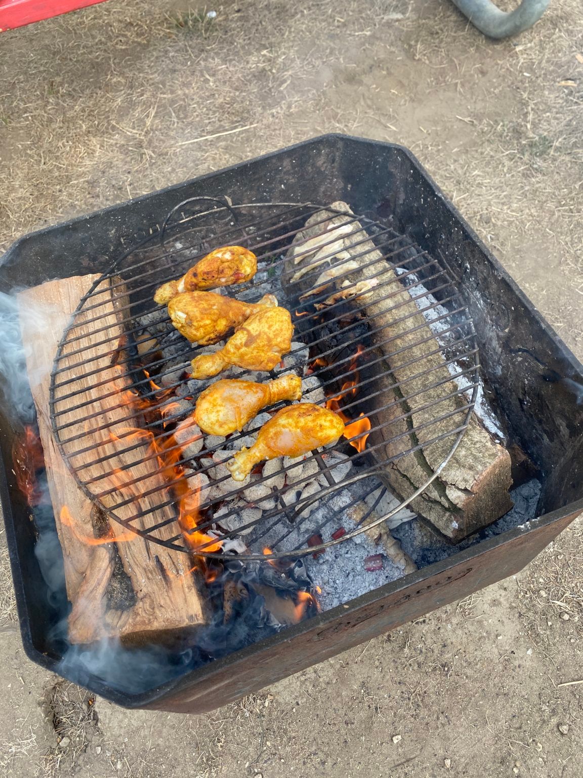 Chicken legs are being cooked on a grill over a fire.