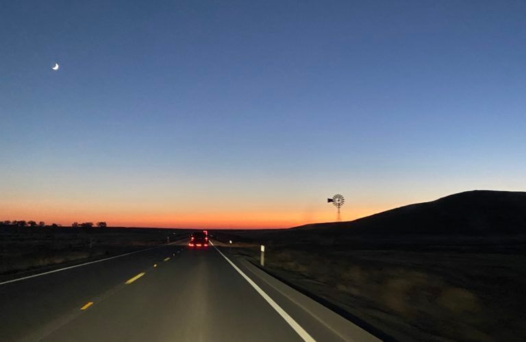 A car is driving down a highway at sunset